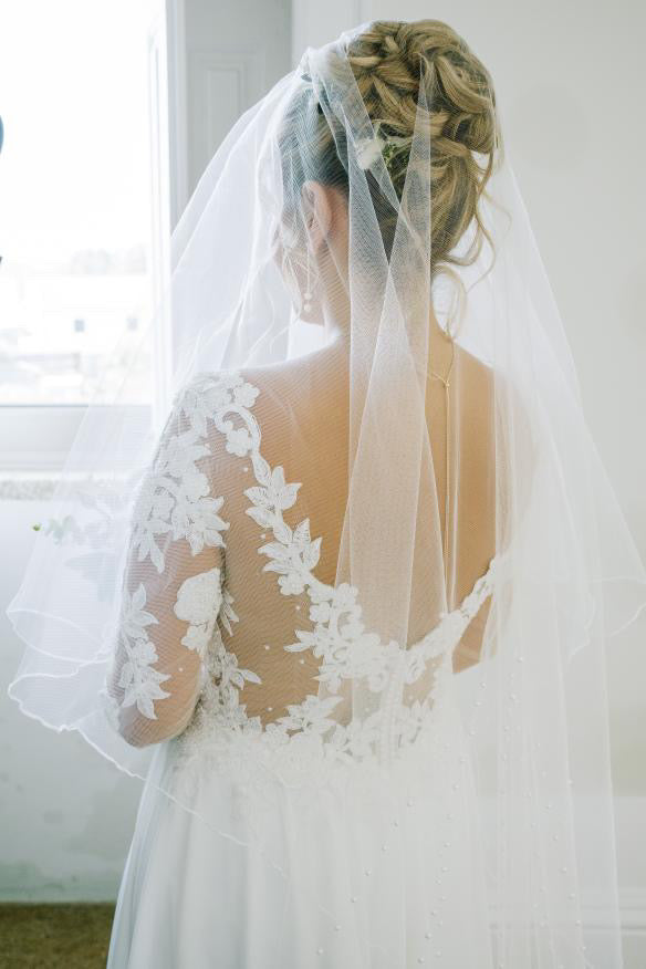 Mariée avec un chignon haut tressé, orné d'un voile de mariée délicat, créant une coiffure nuptiale élégante et romantique pour un mariage enchanteur.