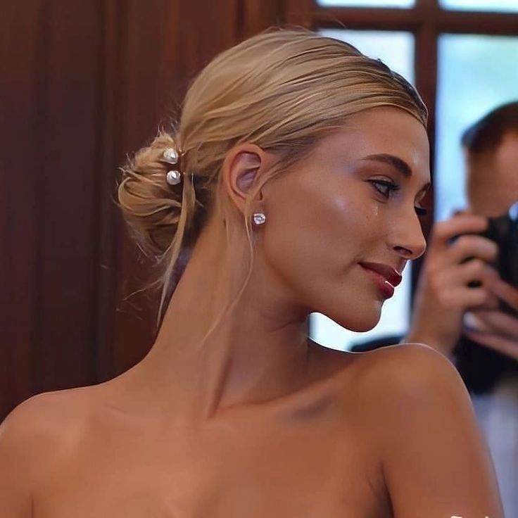 Hailey Bieber rayonnant avec un chignon de mariage chic et sophistiqué, ornée de délicats accessoires qui ajoutent une touche de glamour. Cette coiffure met en valeur son visage et son élégance, offrant une inspiration parfaite pour les mariées à la recherche d'un look moderne et intemporel pour leur grand jour