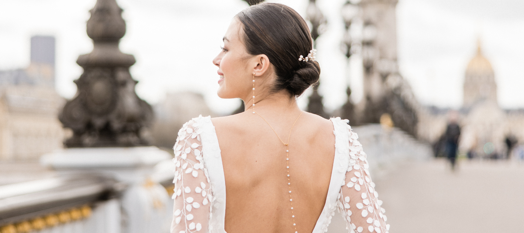 Mariée sur le pont Alexandre III à Paris portant des boucles d'oreilles pendantes à perles, un collier de dos à perles assorties et un pic à cheveux à perles