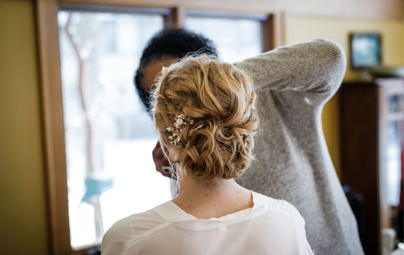 Gros chignon de mariée avec des cheveux bouclés, orné d'un bijou éclatant qui sublime la coiffure, créant un look nuptial magnifique et romantique.