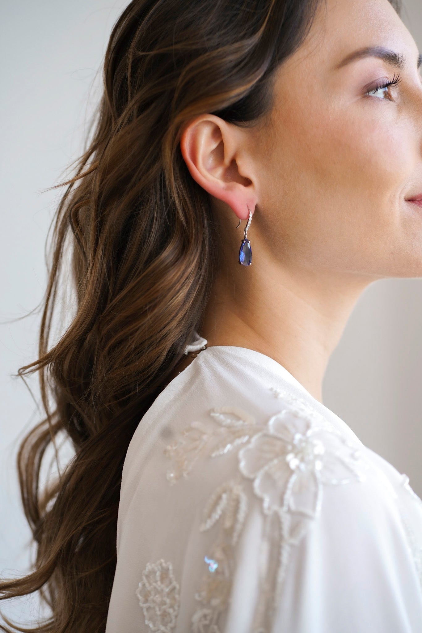 Mariée de profil avec de longs cheveux bouclés portant des boucles d'oreilles de pierre bleue