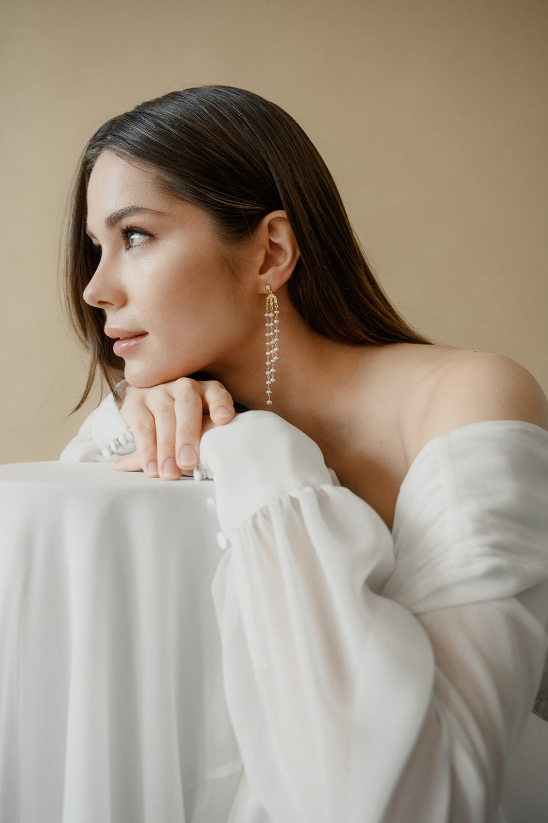 Femme de profil qui a sa tête posée sur ses mains permettant de voir ces bijoux de cérémonies à fines perles naturelles pendantes à plusieurs rangs
