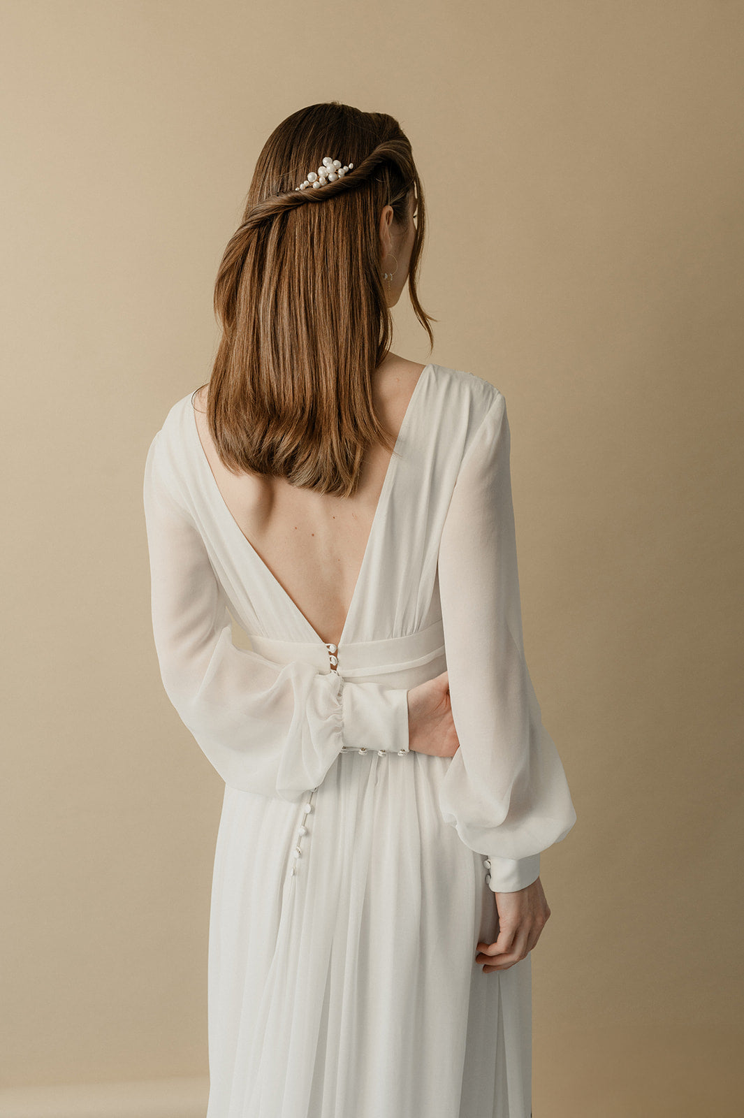 femme debout de dos portant une robe de mariée manche longue et un accessoire de cheveux