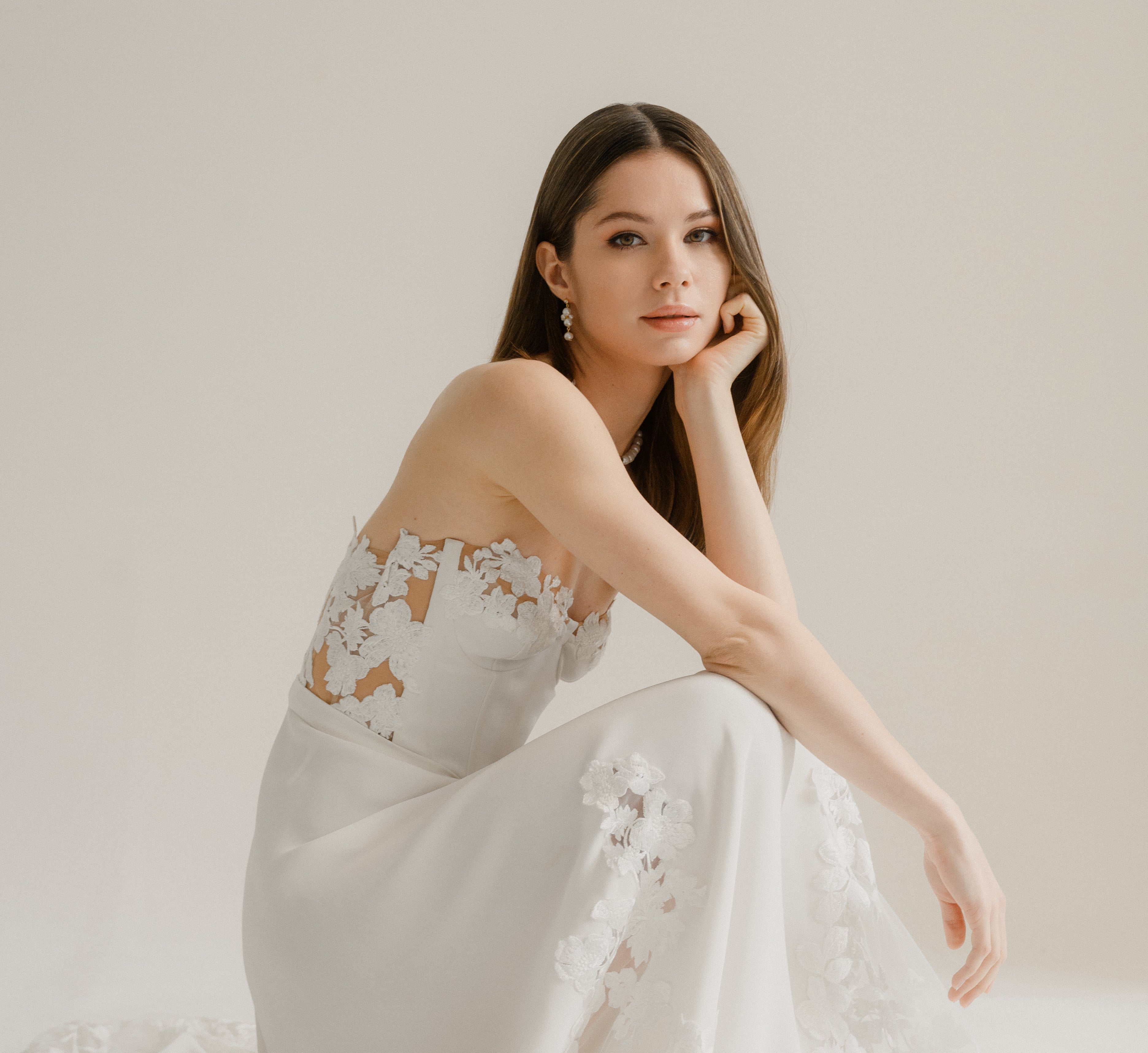 Femme accroupie portant une robe et des bijoux de mariées notamment des boucles d'oreilles en perles naturelles pendantes