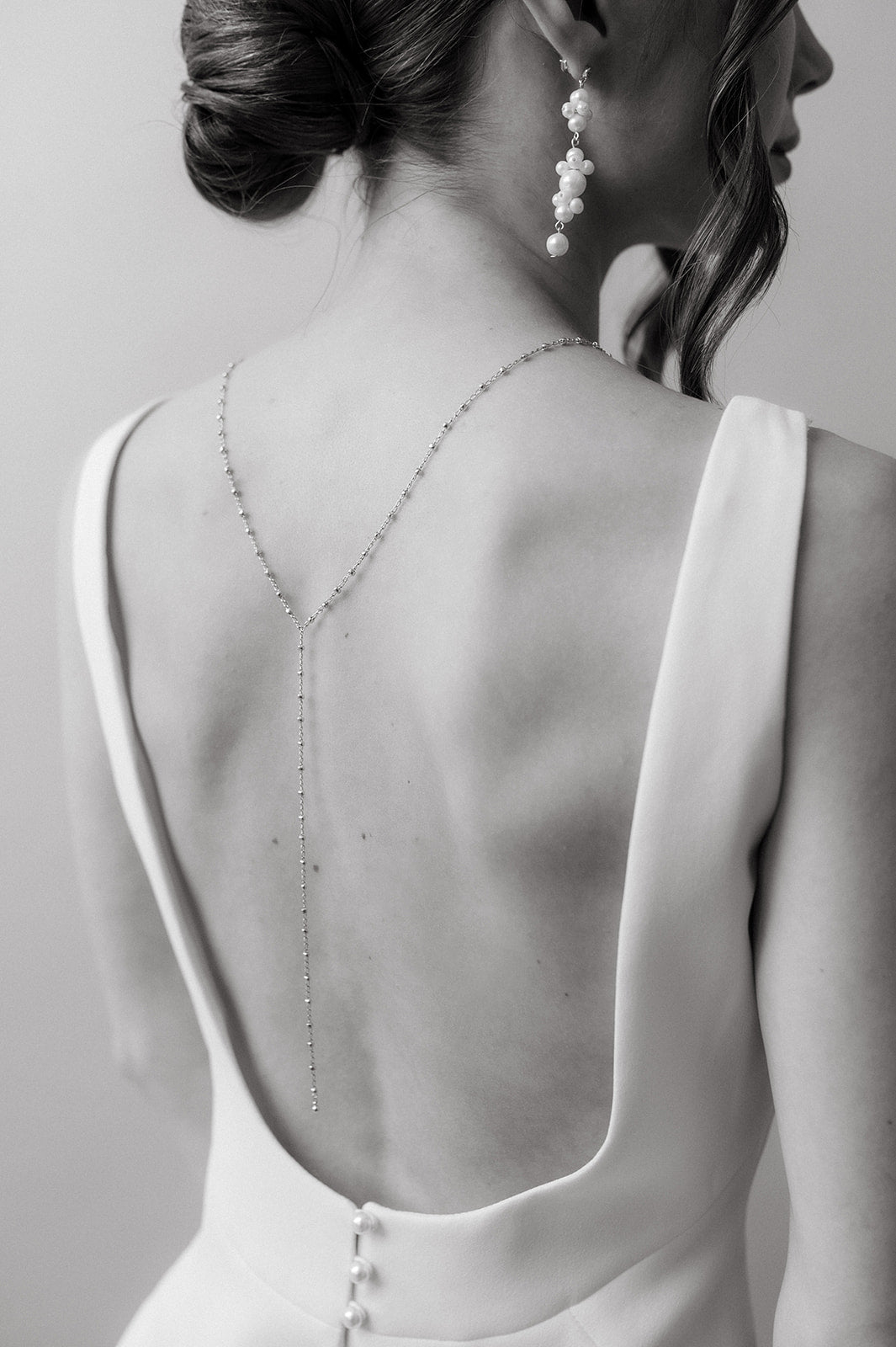 femme de dos en noir et blanc portant un collier de dos avec une chaine perlée et des boucles d'oreilles en perles naturelles