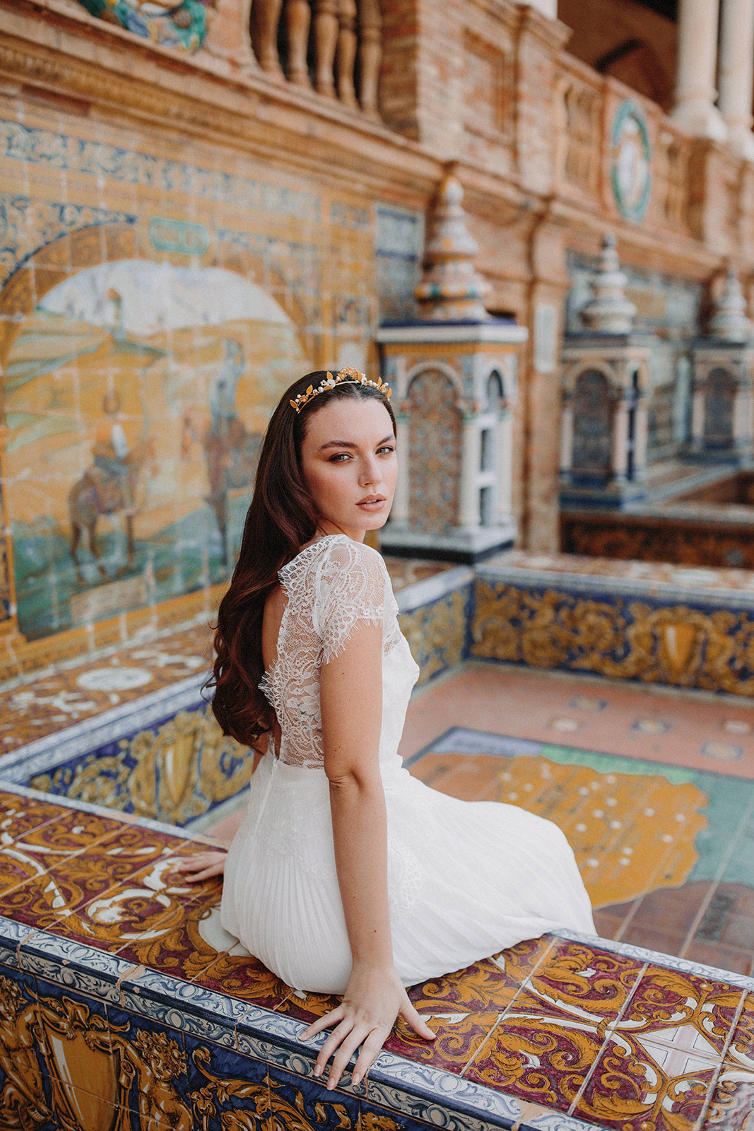 Mariée assise sur un banc de carreaux peint en robe de mariée en dentelle avec une couronne dorée