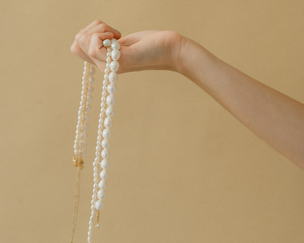 Photo d'une femme tenant des colliers de perles naturelles de mariage dans les mains avec derrière un fond unis