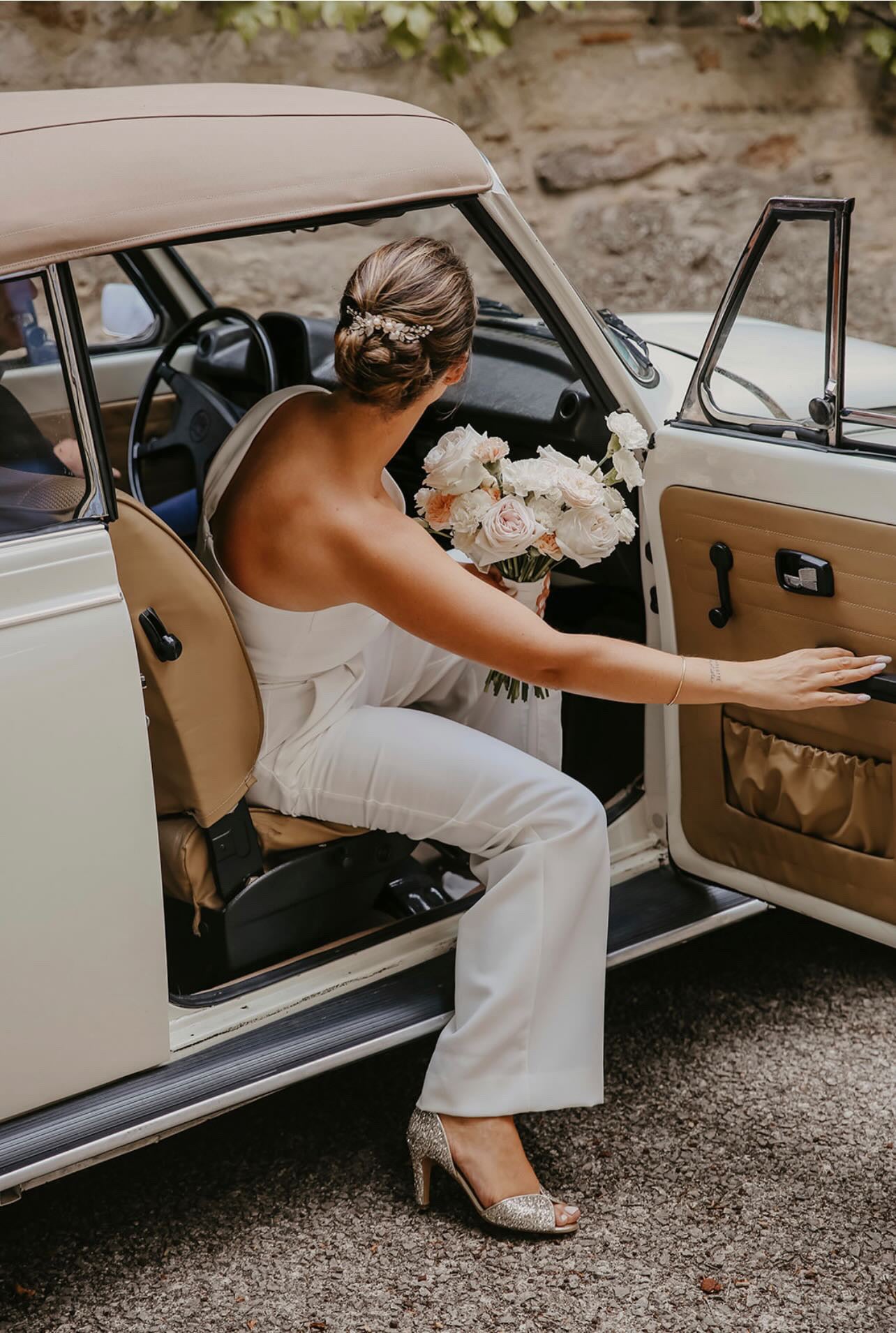 Mariée avec un chignon élégant vu de dos, sortant d'une voiture, mettant en avant sa coiffure raffinée et son style nuptial, parfaite pour un mariage chic et mémorable.