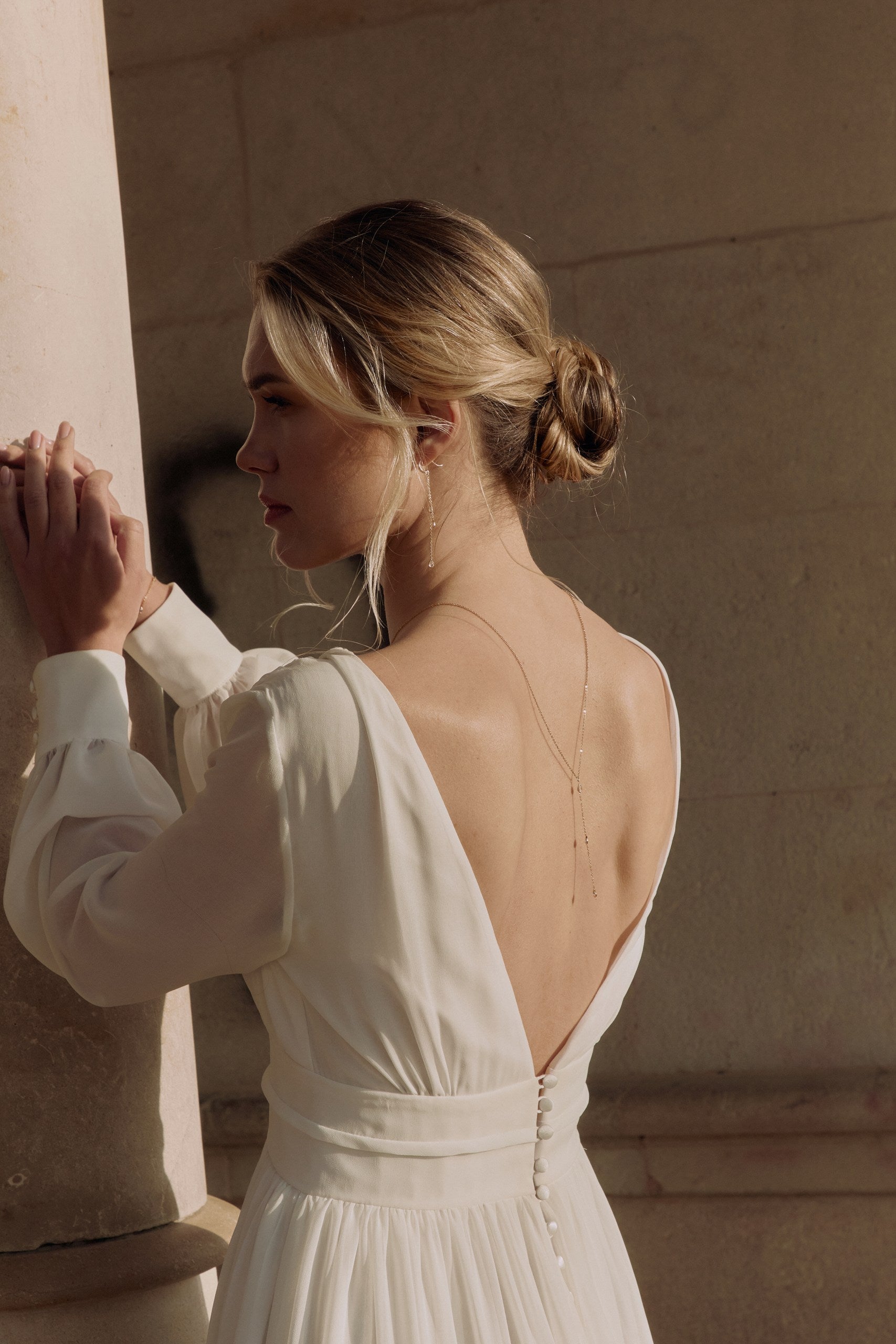 mariée de dos portant une robe blanche avec des manches longues et une parure de bijoux assortie en perles naturelles