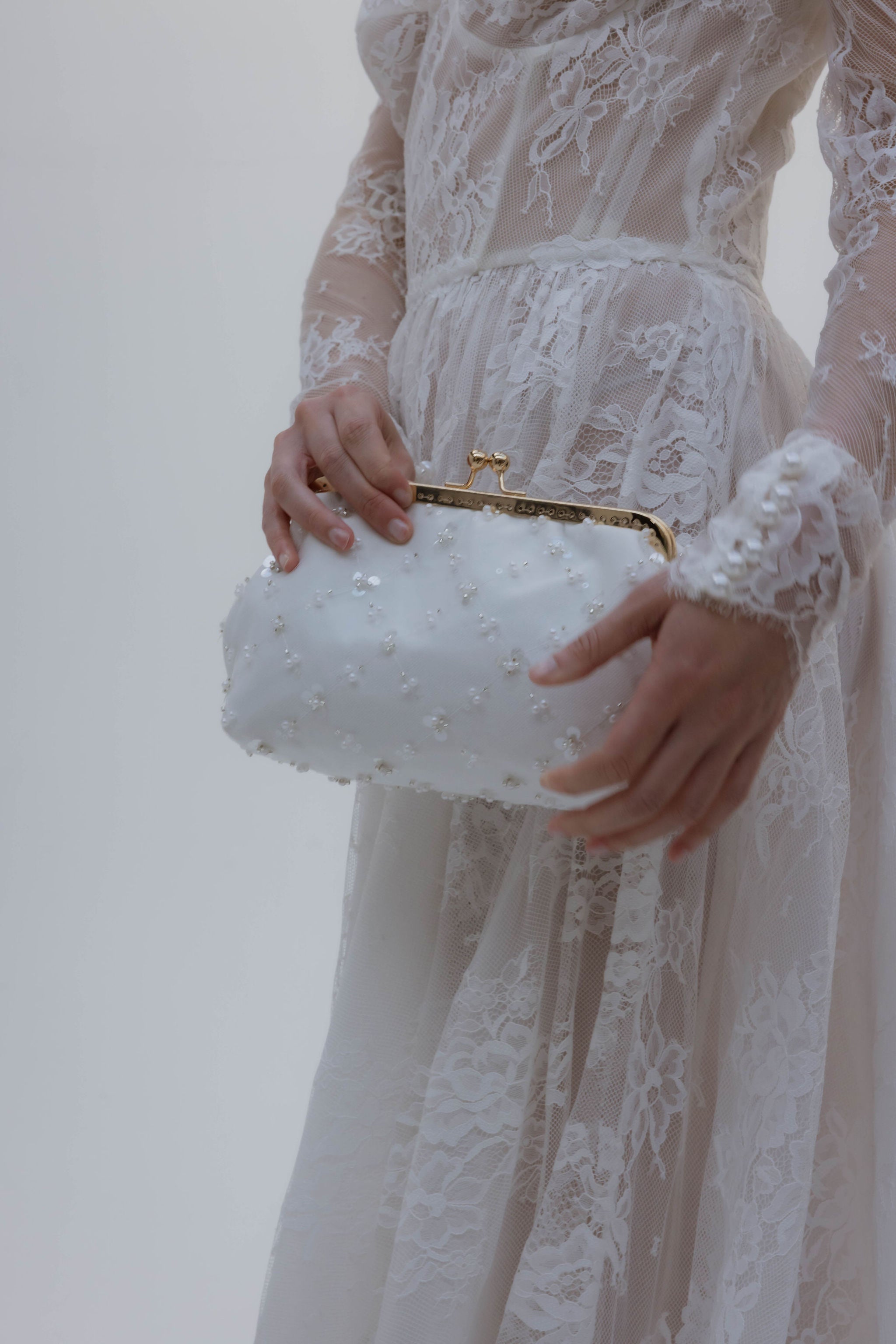Sac blanc tenu par la mariée, qui porte une robe manches longues en dentelle.