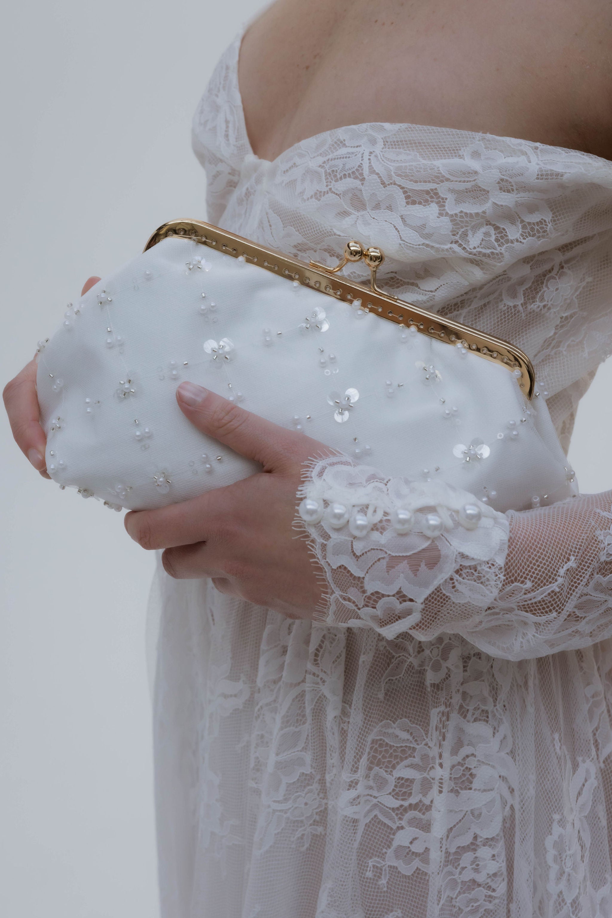 Sac blanc tenu par la mariée, qui porte une robe bustier en dentelle avec manches longues.