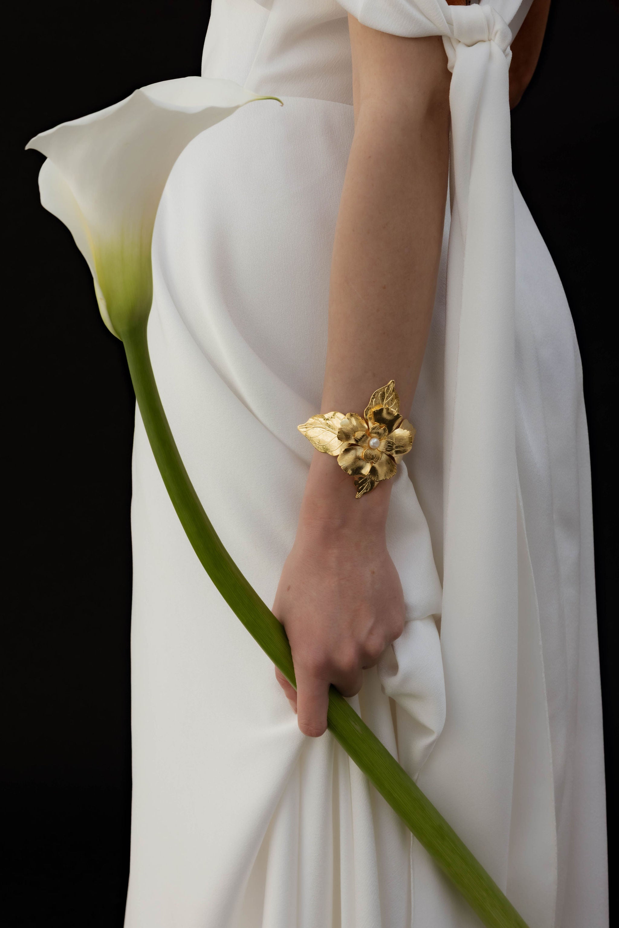 Mariée portant un gros bracelet floral avec des perles au centre, tenant une fleur dans sa main, pour un look élégant et romantique.