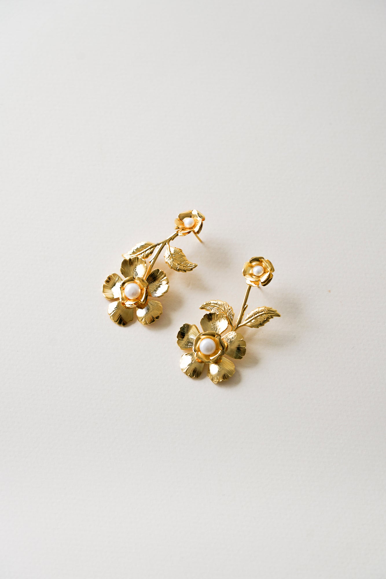 grandes boucles d'oreilles florales dorées ornes de perles sur un fond blanc