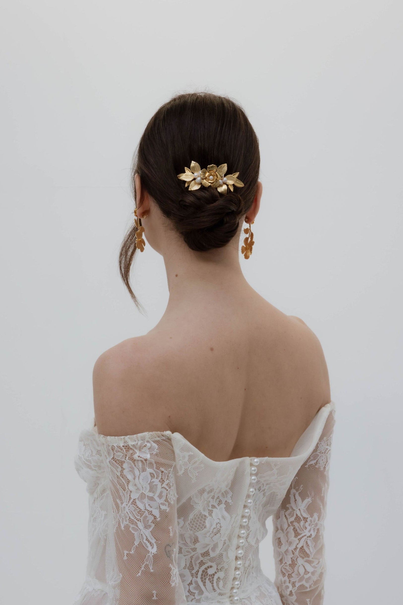 Mariée de dos qui porte un accessoire floral dore avec des perles de culture sur son chignon