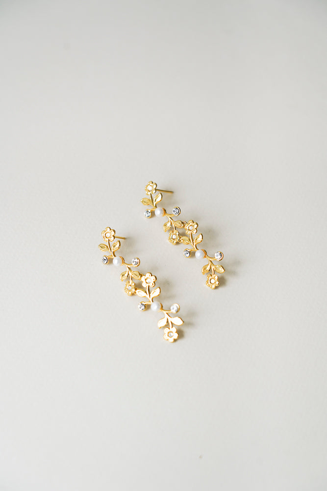 Boucles d'oreilles longues pendantes florales pour mariee avec perles naturelles et cristaux sur un fond beige