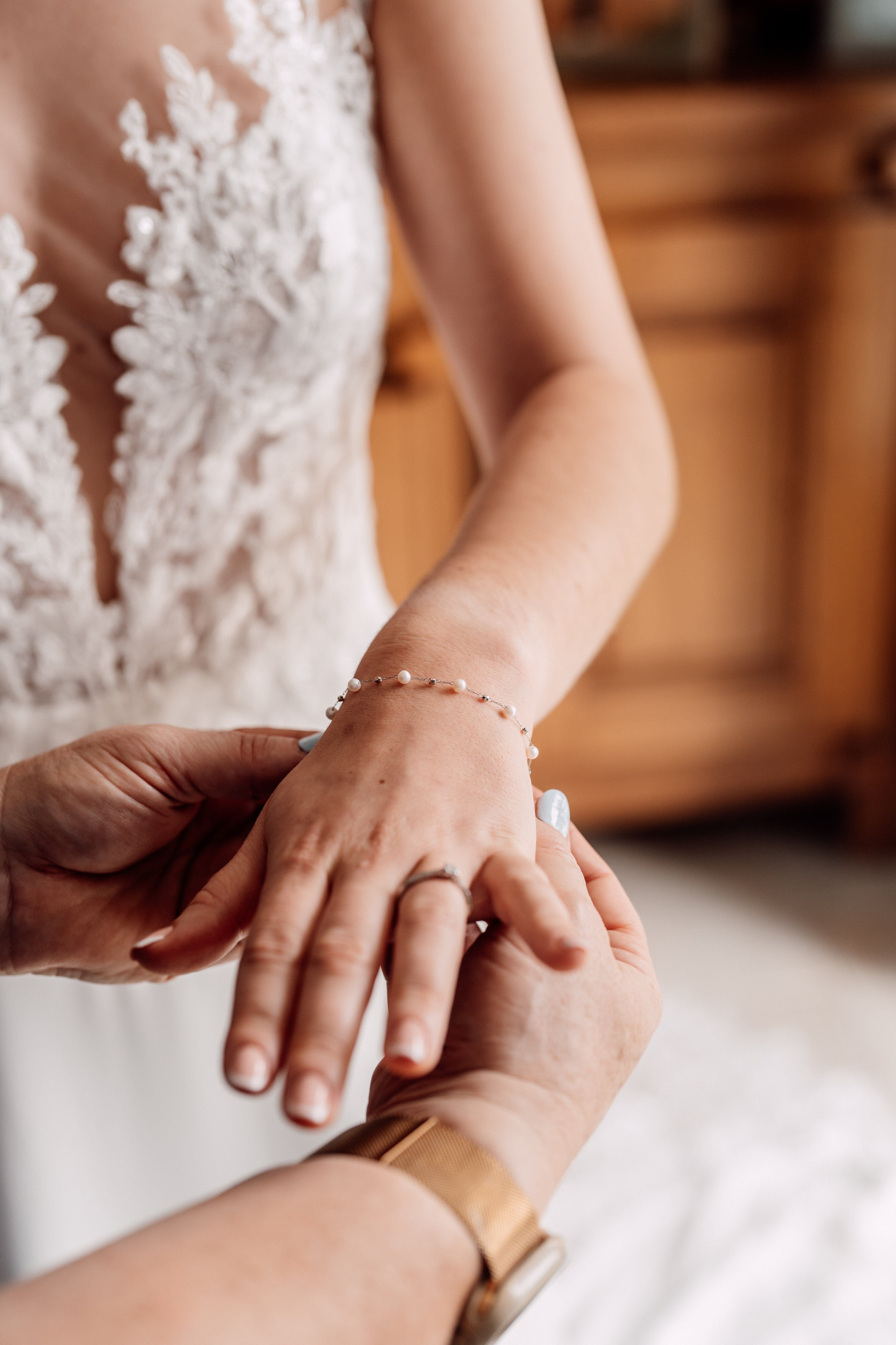 Mariée qui met un bracelet en perles de la marque Atelier Lilac, elle porte une robe de mariage en dentelle