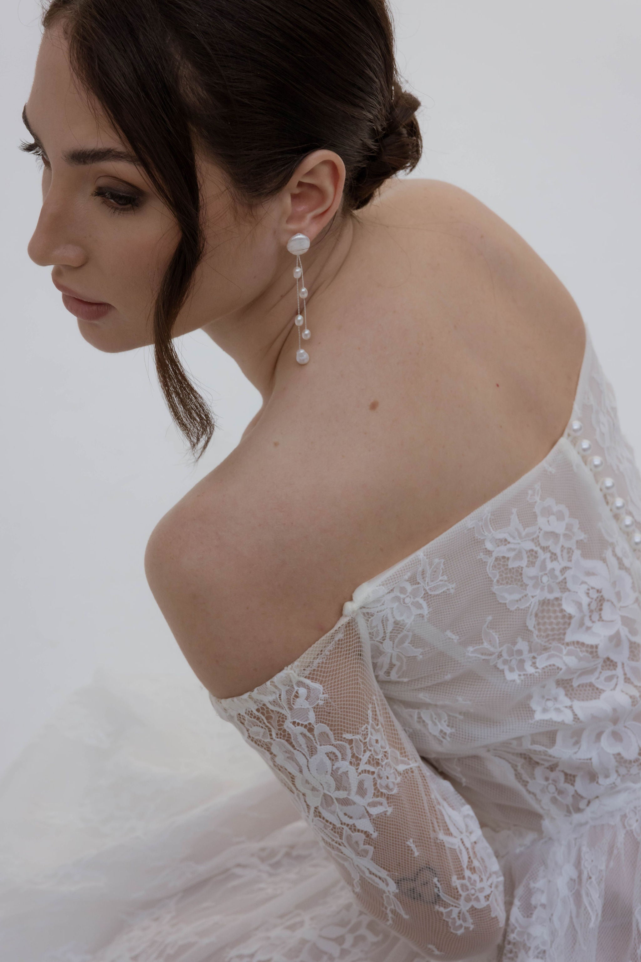 Mariée portant une jolie robe blanche en dentelle et de longues boucles d’oreilles ornées de perles de différentes tailles