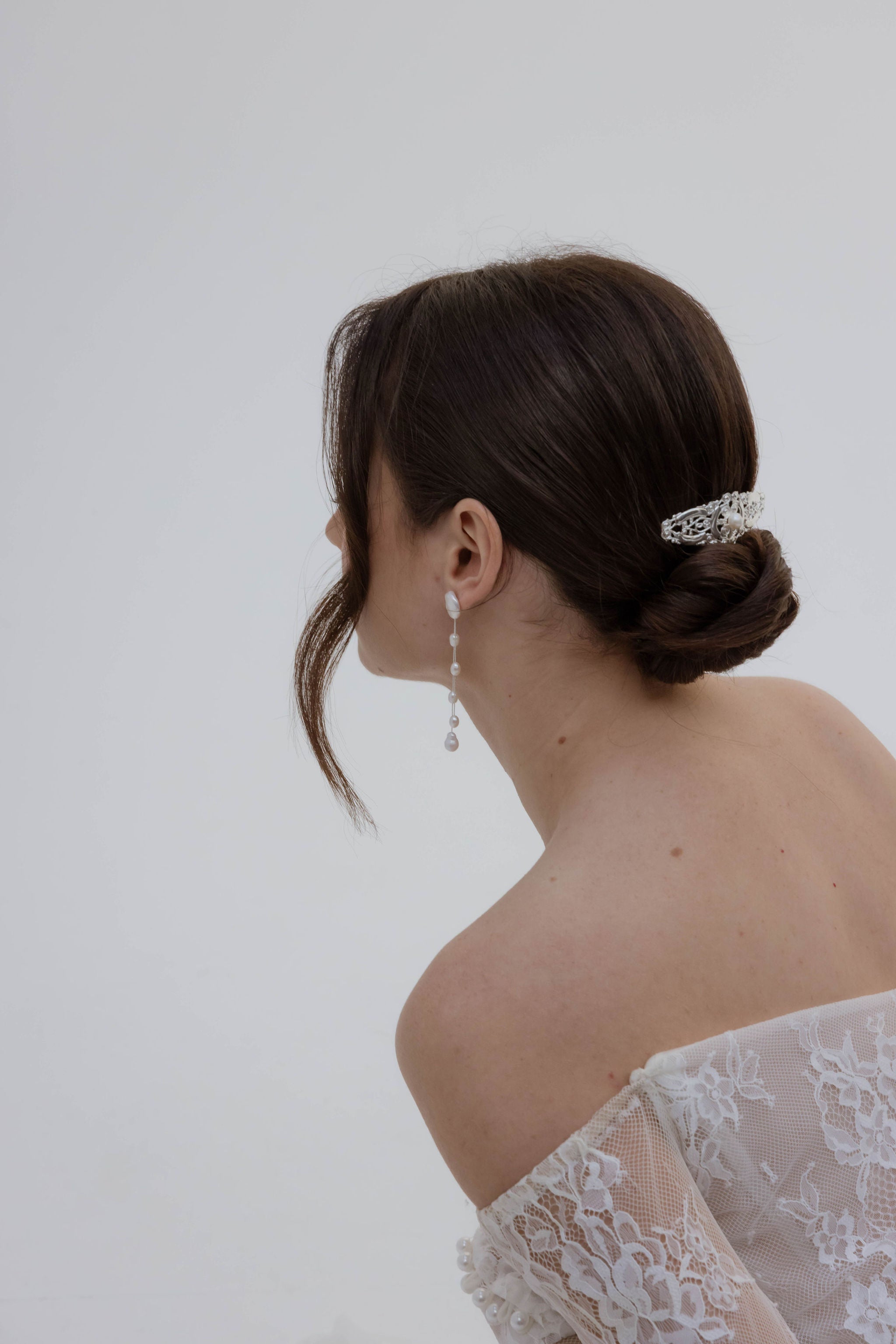 Mariée vue de dos avec un chignon bas décoré d’un pic romantique, portant une robe en dentelle avec manches longues et bustier.