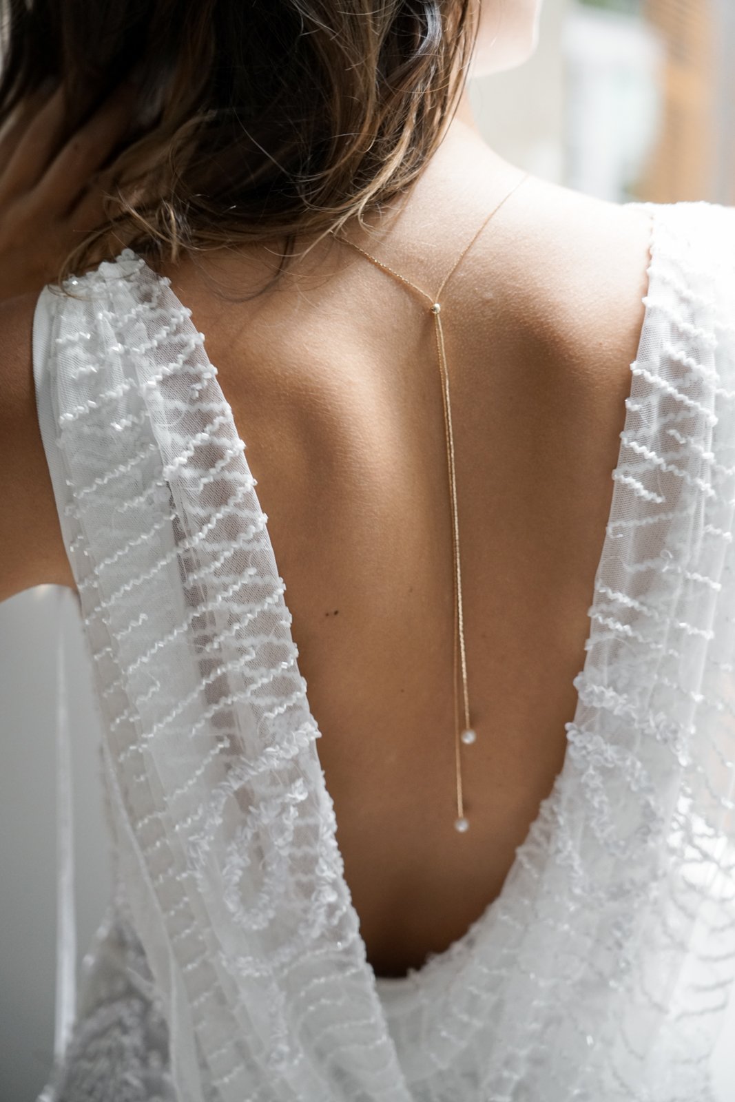 Mariée portant un collier de dos minimaliste doré ajustable avec une double chaine doré et deux perles blanches au bout de chacune