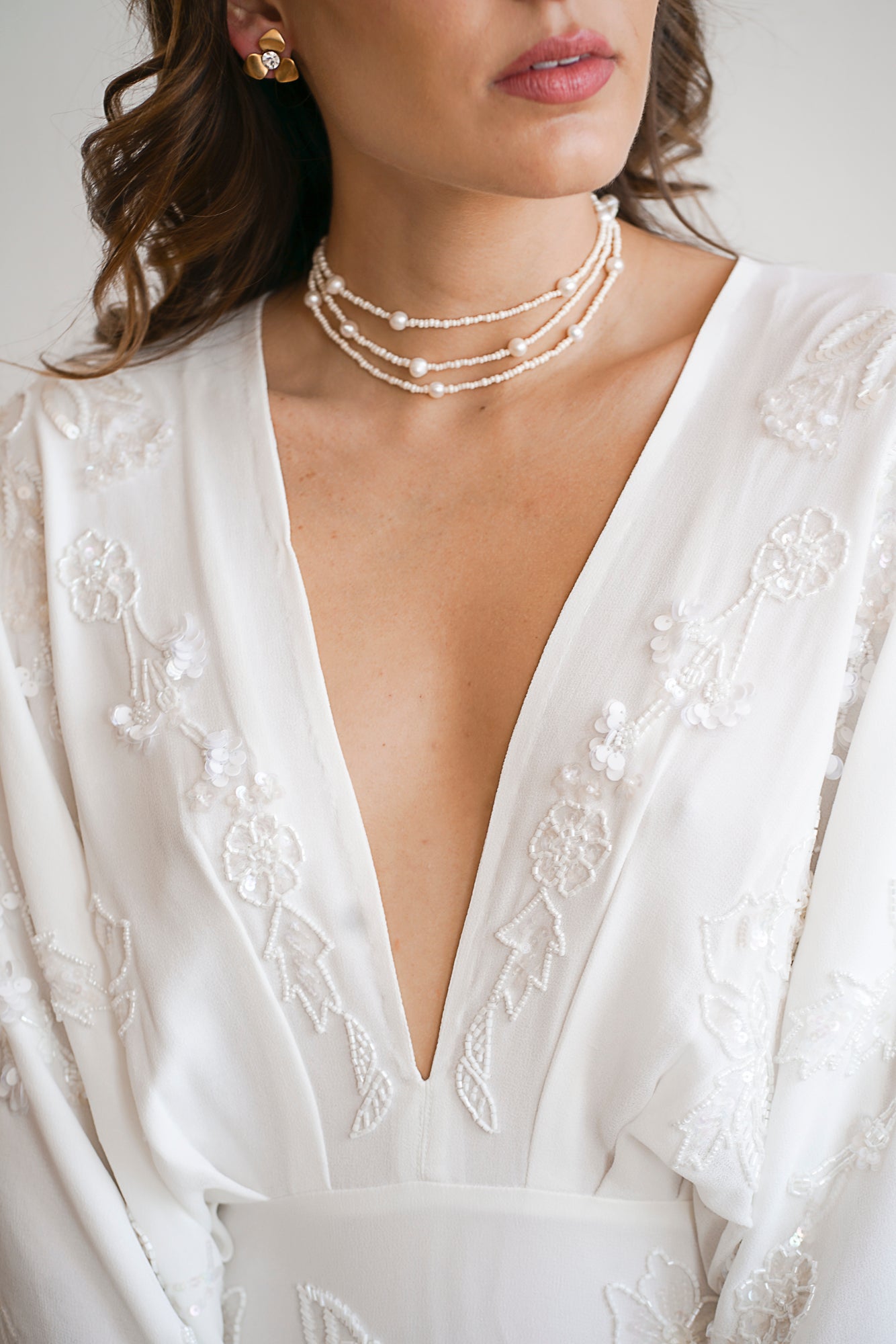 Mariée portant un collier à trois rangs fait de perles rocailles et de perles naturelles avec des boucles d'oreilles fleurs dorées