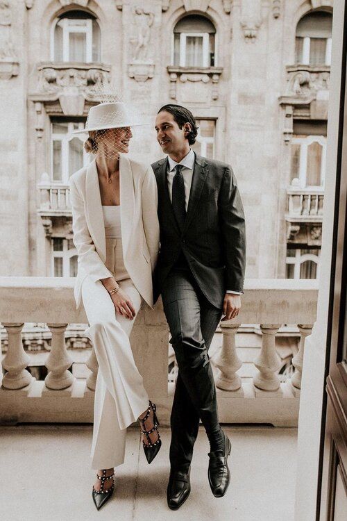 couple qui se regarde, la mariée est moderne et porte un pantalon ainsi qu'un chapeau voile de mariage.