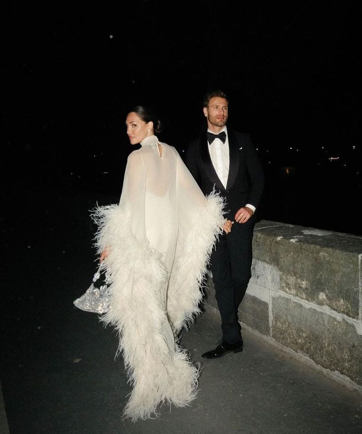 Couple qui marche après leur mariage hivernal, la mariée porte une cape avec des plumes et un sac de mariee