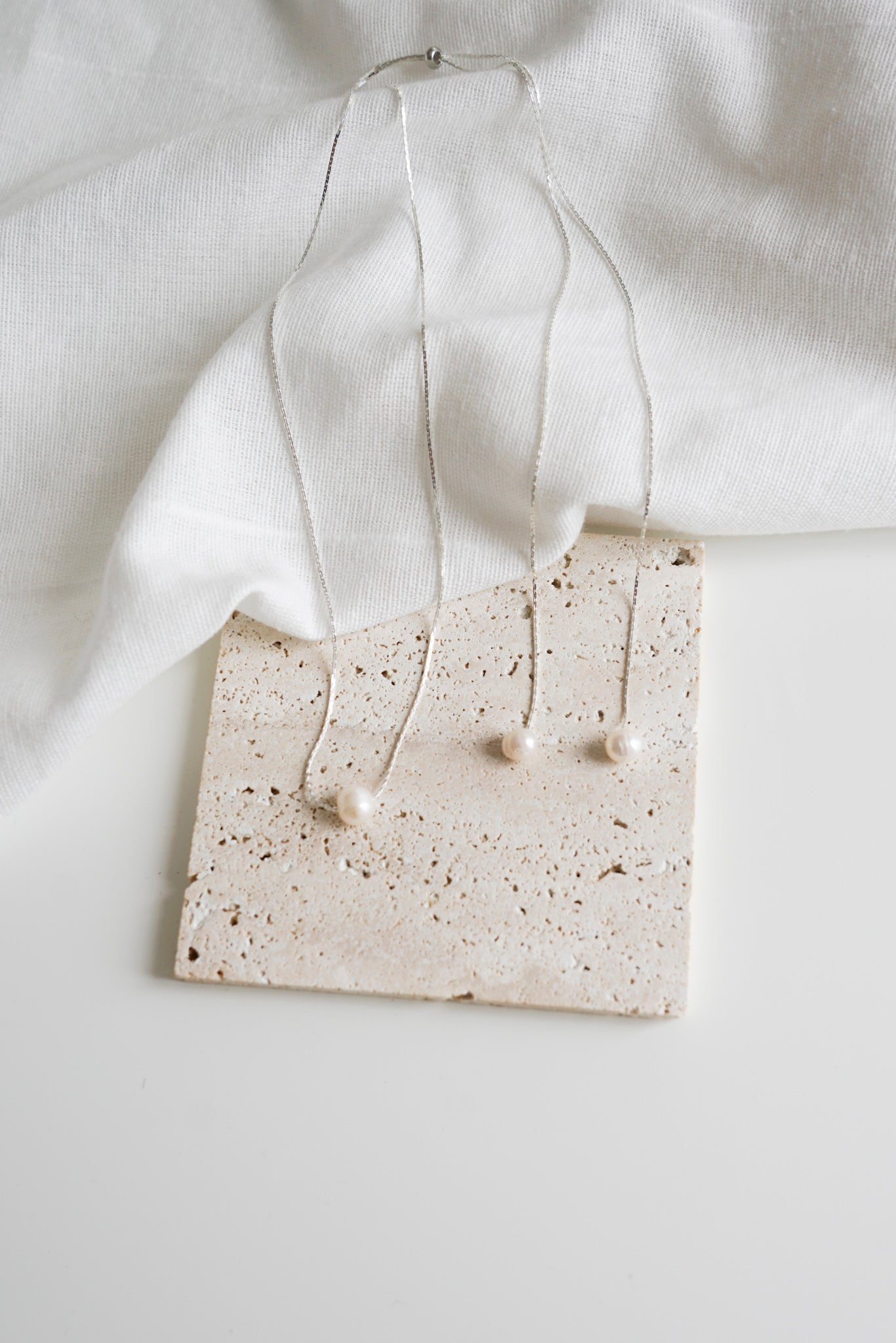 collier de dos pour mariage sur une pierre carré beige et un drap blanc en lin