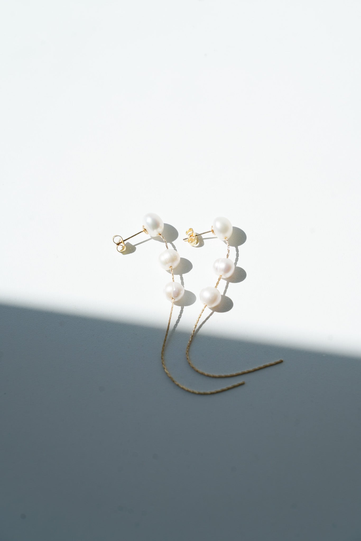 boucles d'oreilles pendantes posé sur une table avec une ombre qui se reflète