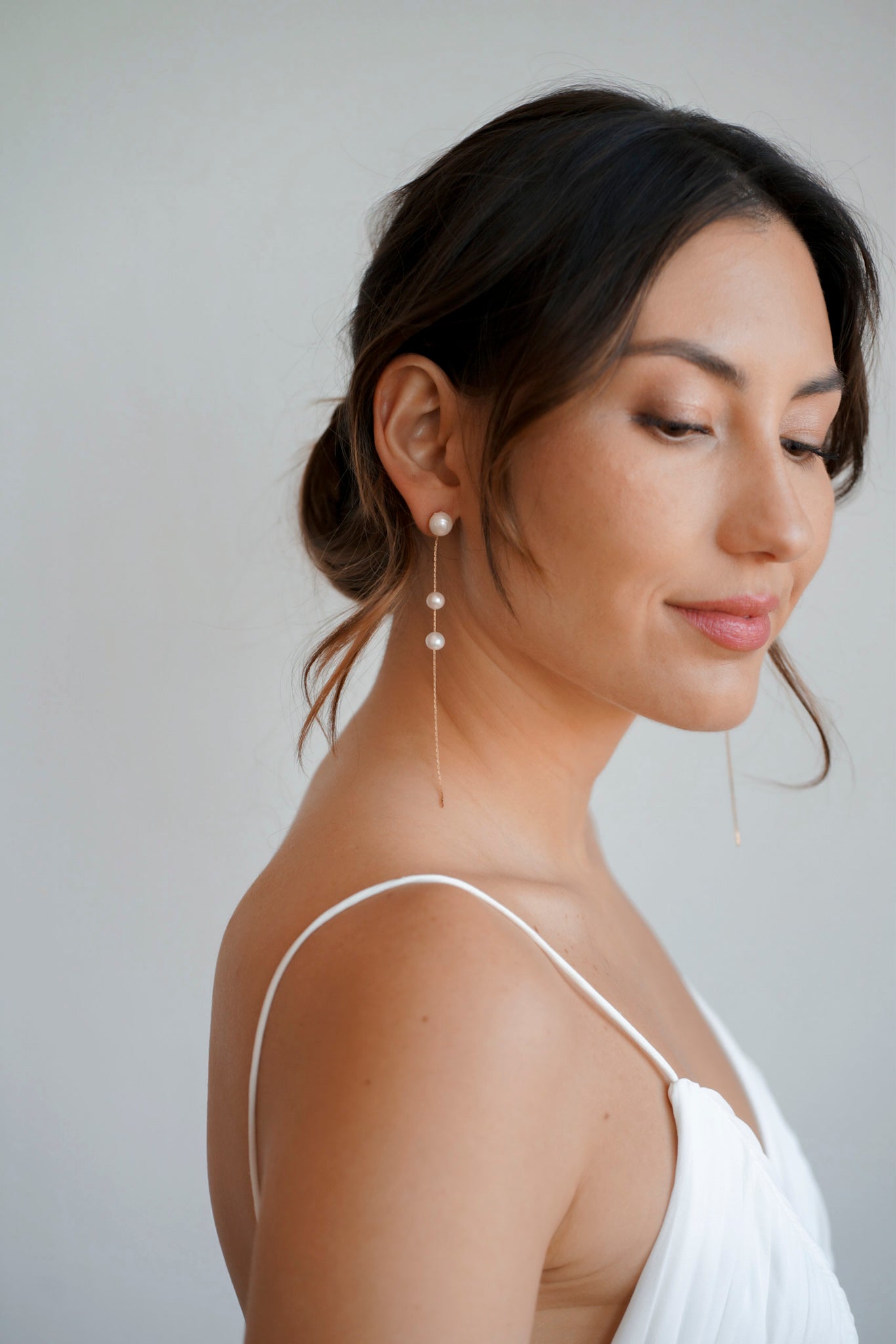 Boucles d'oreilles pendantes en or avec 3 perles blanches portées par une femme avec un chignon de mariage