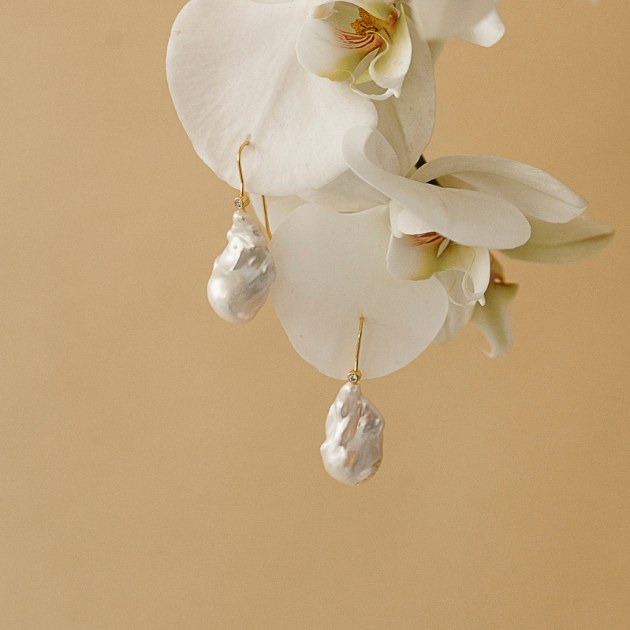 Boucles d'oreilles en perles dorees qui pendent d'une orchidée blanche.