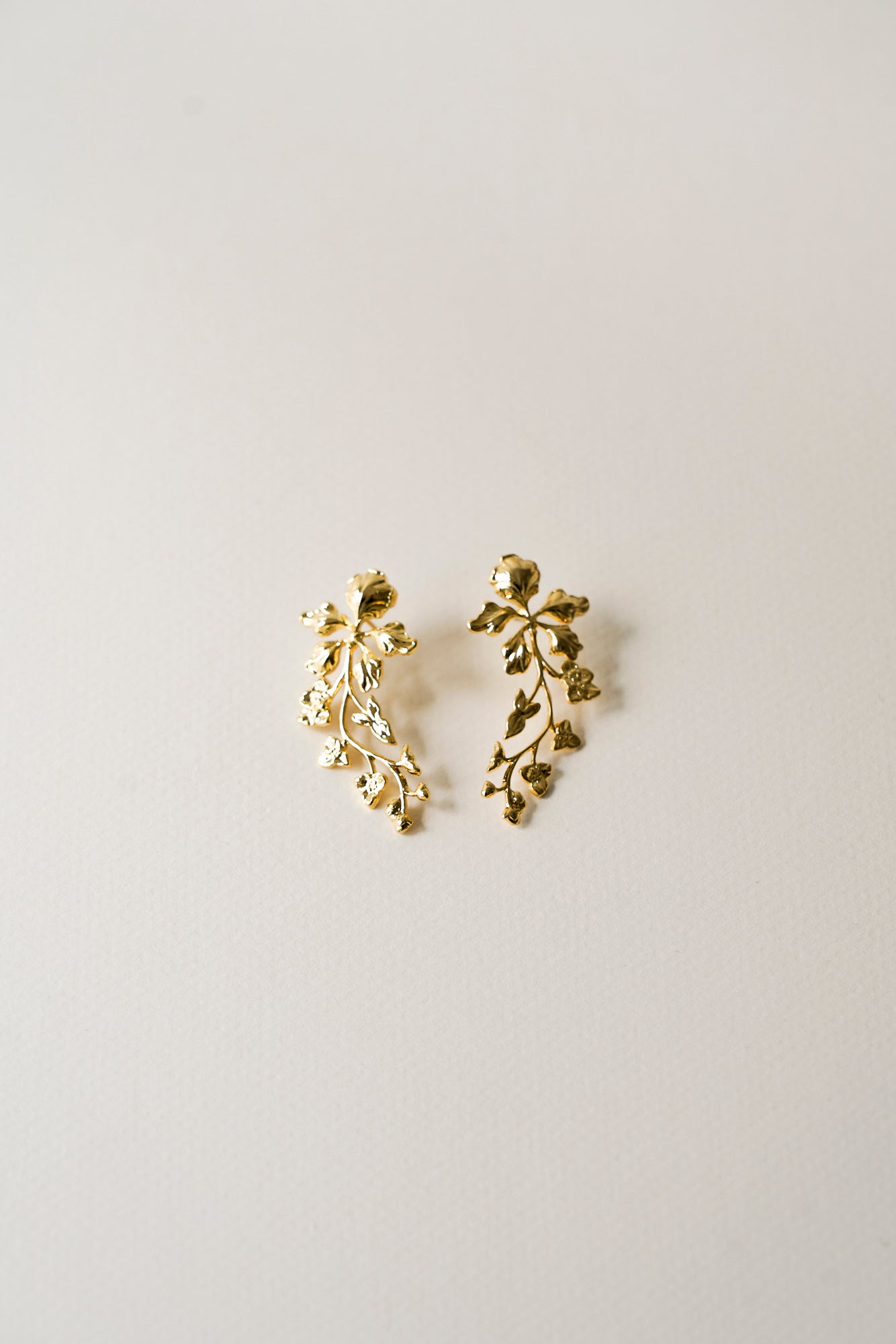Boucles d'oreilles florales romantique dorées sur un fond beige clair