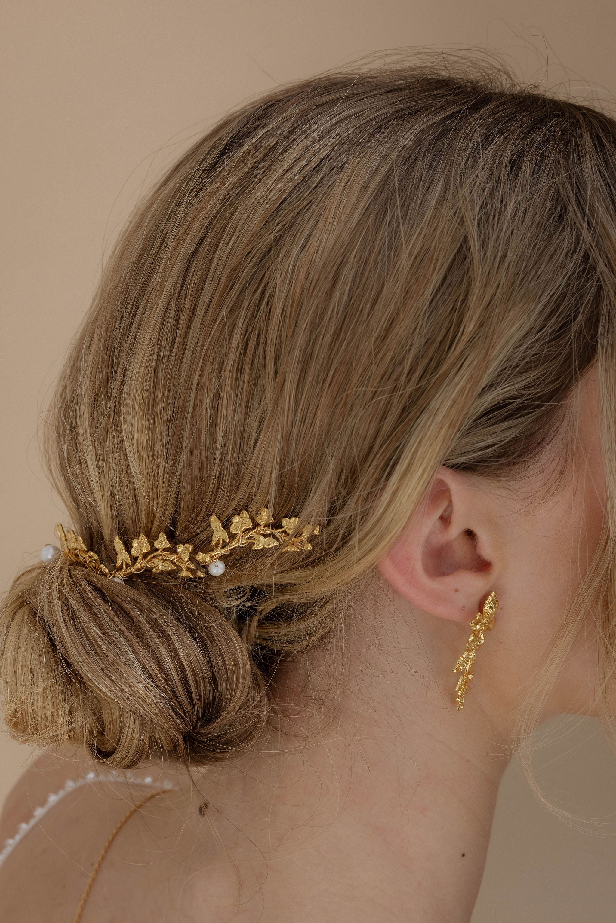 Chignon de mariée orné d’un accessoire de cheveux en or, au style romantique et floral, parfait pour un mariage élégant.