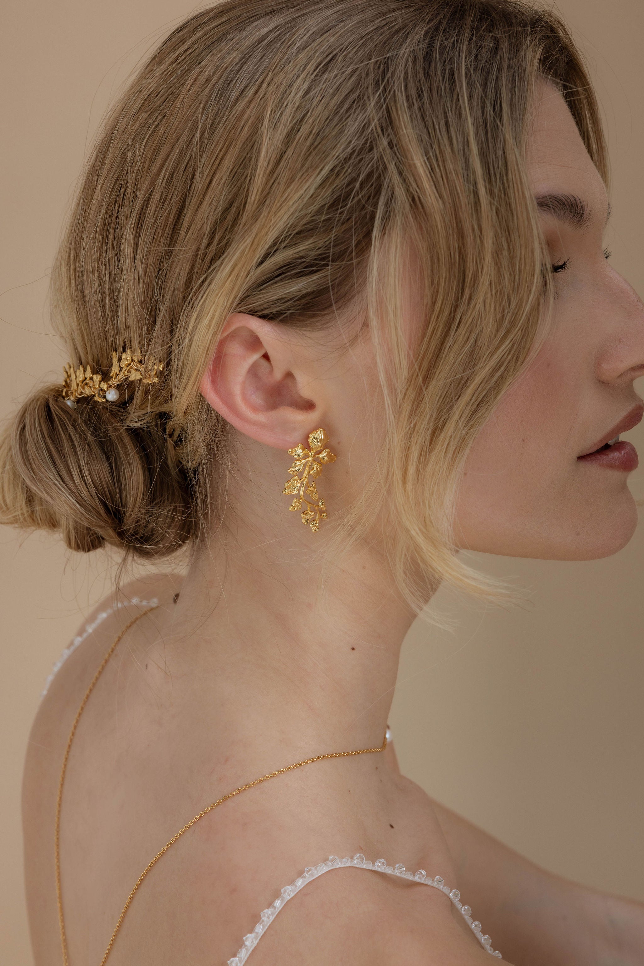 Boucles d'oreilles longues florales, idéales pour une mariée avec un chignon élégant, accompagnées d'accessoires pour cheveux qui ajoutent une touche romantique et sophistiquée à sa coiffure.