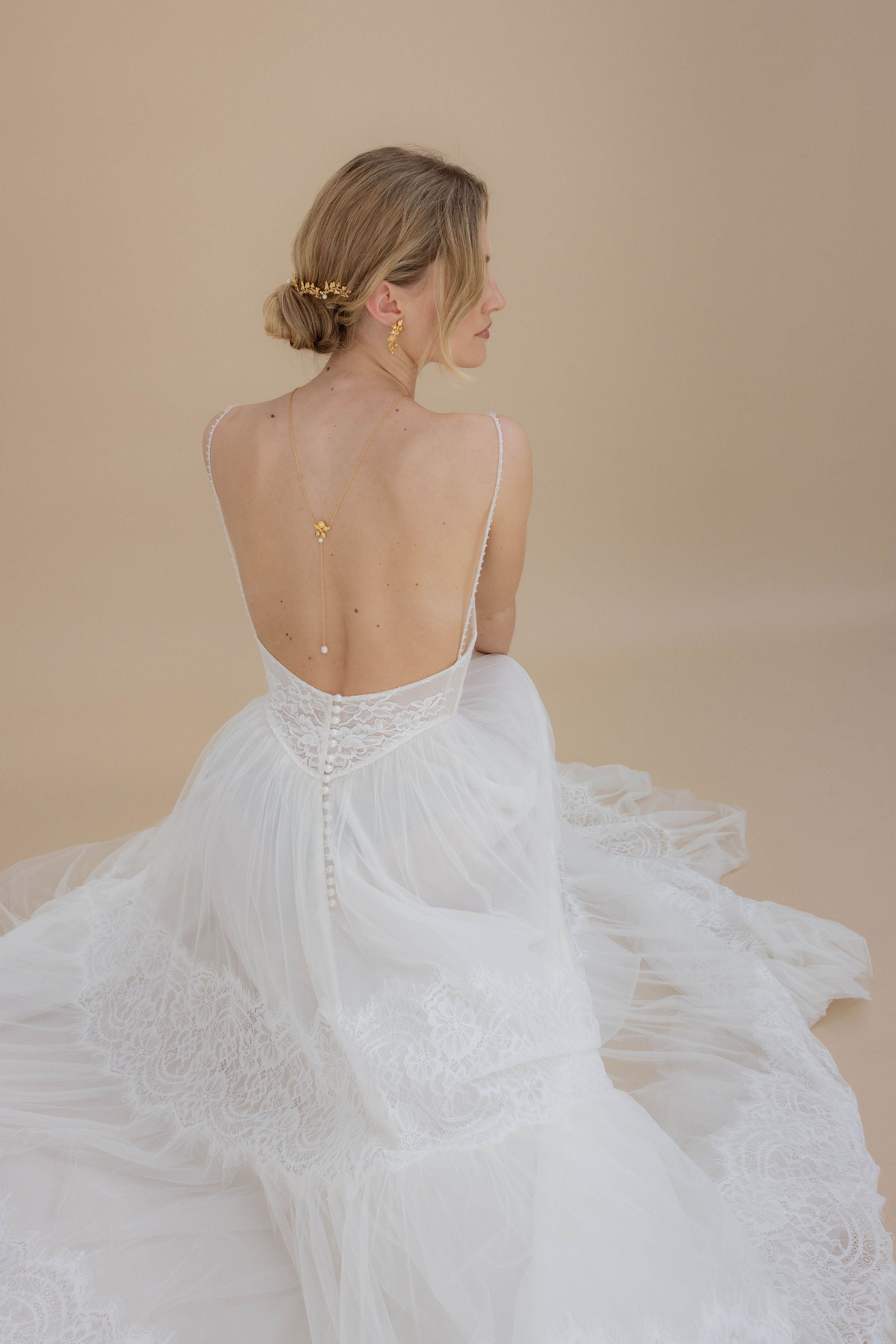 Collier de dos délicat associé à des boucles d'oreilles florales, créant un look harmonieux et élégant pour la mariée, avec des perles et des détails floraux qui subliment le décolleté et ajoutent une touche romantique.