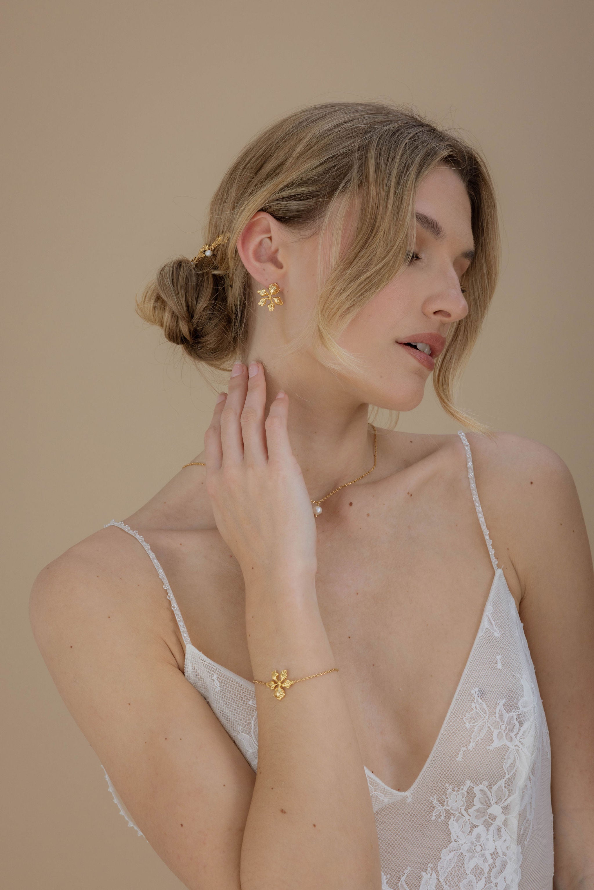 Mariée avec un chignon de mariage élégant, portant des boucles d'oreilles courtes en doré et des accessoires floraux pour une touche romantique et délicate à son look de mariage.