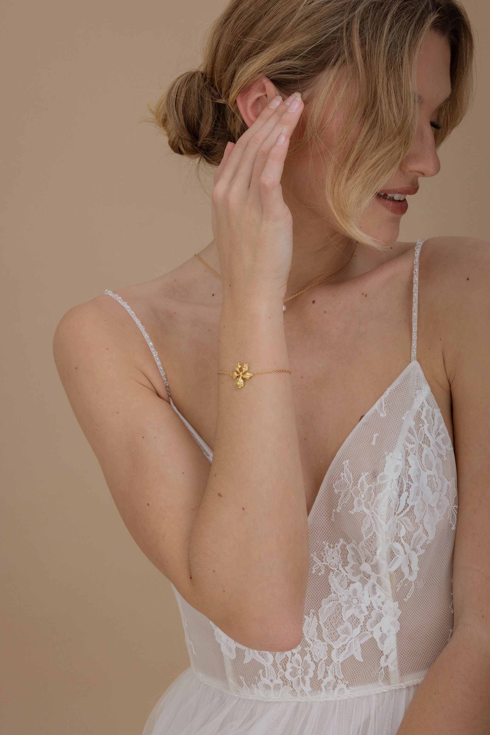 Mariée en robe blanche élégante, accessoirisée d’un bracelet fin en or avec fleur délicate, pour un style doux et féminin.