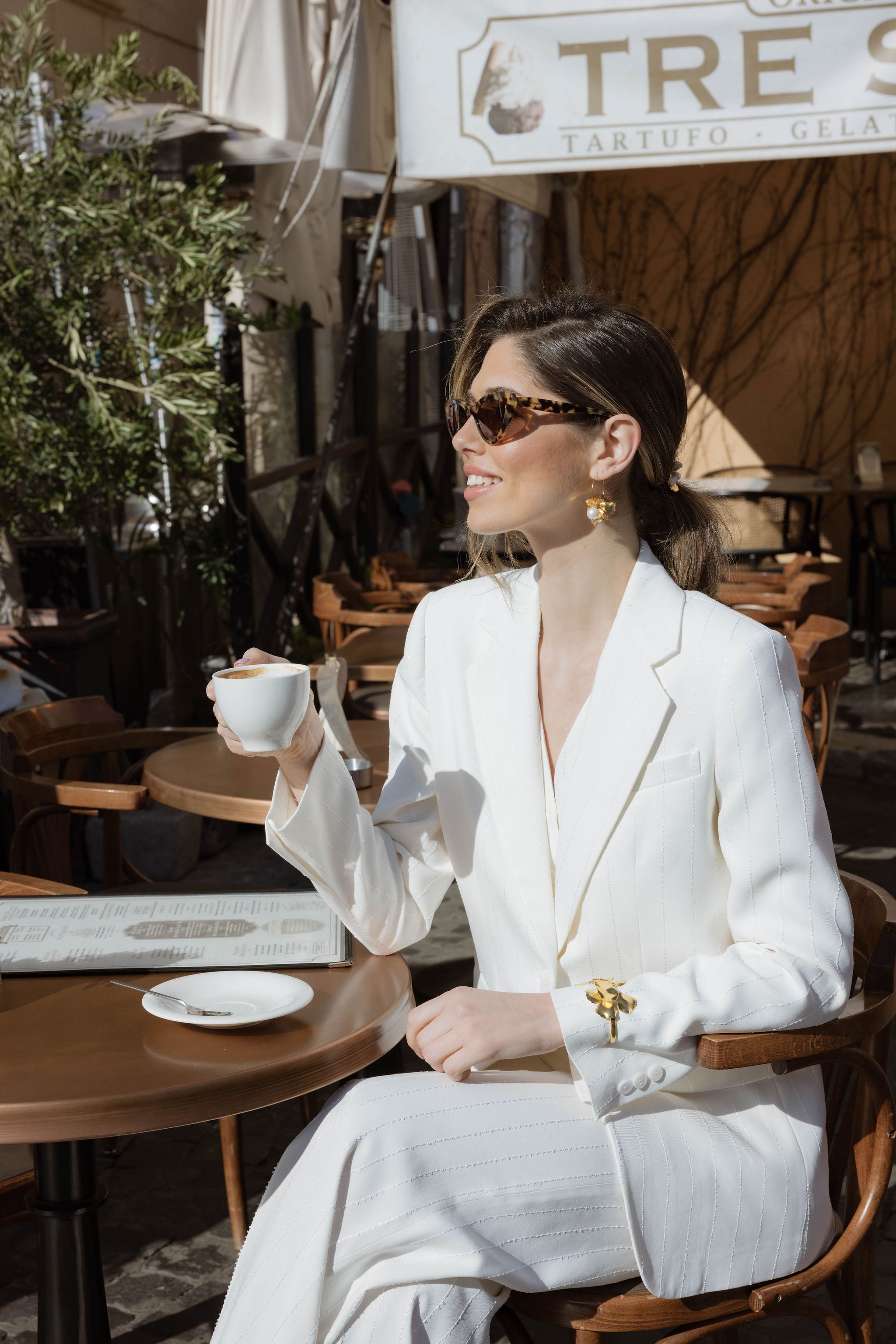 Mariée de profil souriant en buvant son café portant un bracelet floral de mariage au dessus de son costume pour mariée