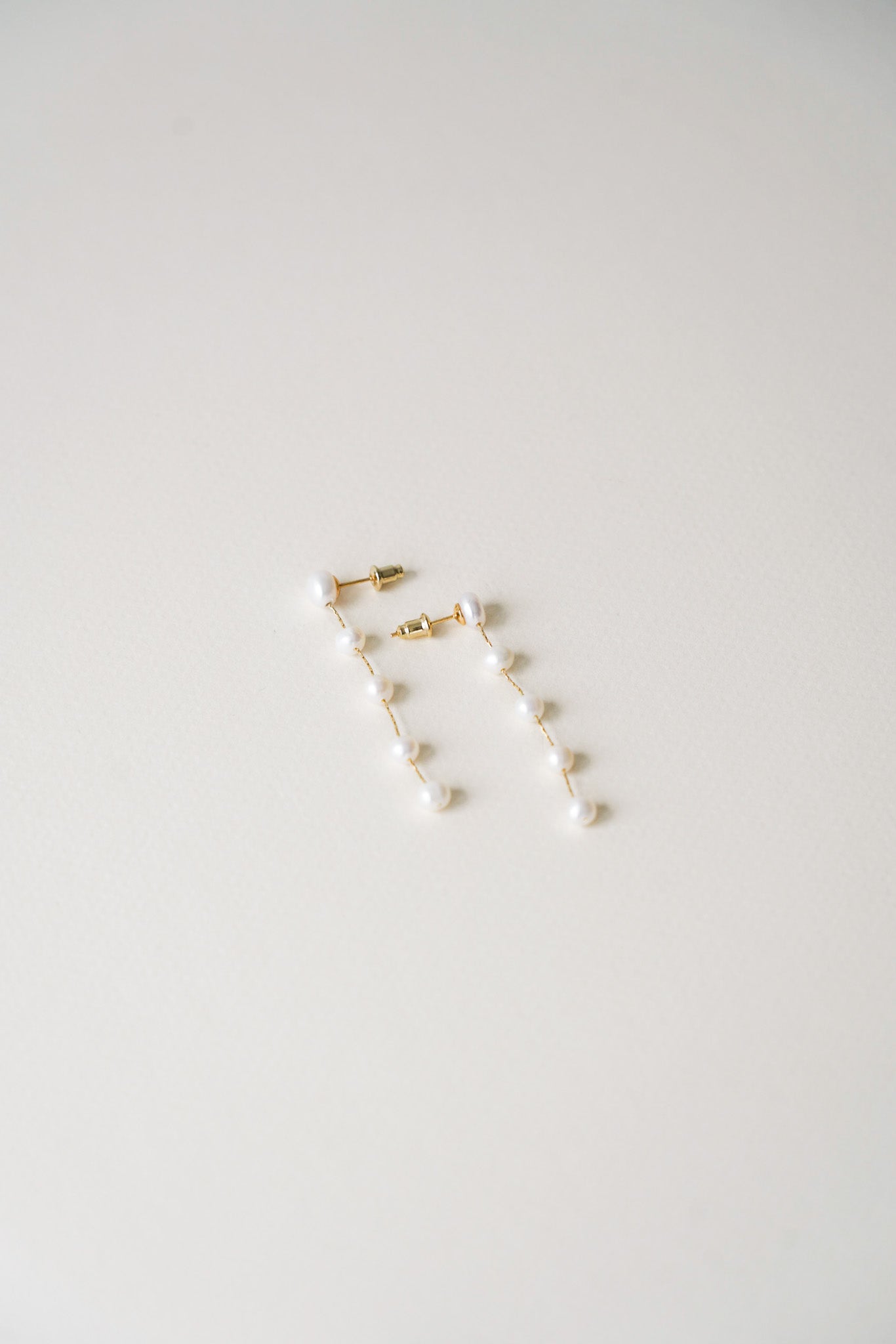 Boucles d’oreilles longues élégantes, composées de cinq perles de culture blanches en enfilade. Chaque perle, délicatement espacée, crée un effet léger et raffiné, parfait pour sublimer une tenue de mariage ou une occasion spéciale. Un bijou intemporel alliant simplicité et sophistication.