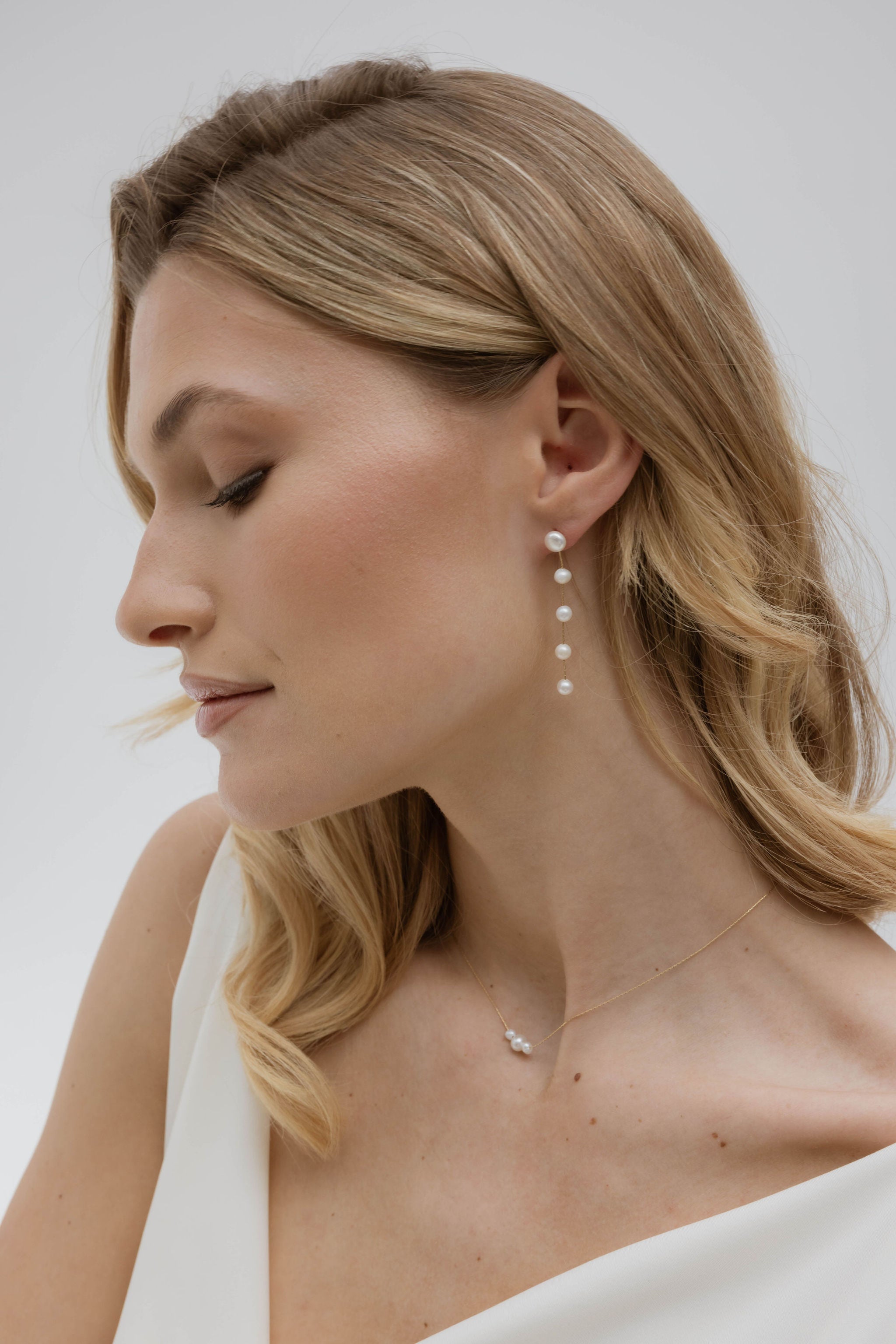 Mariée aux cheveux lâchés, portant de jolies boucles en perles naturelles pour un look délicat et naturel.