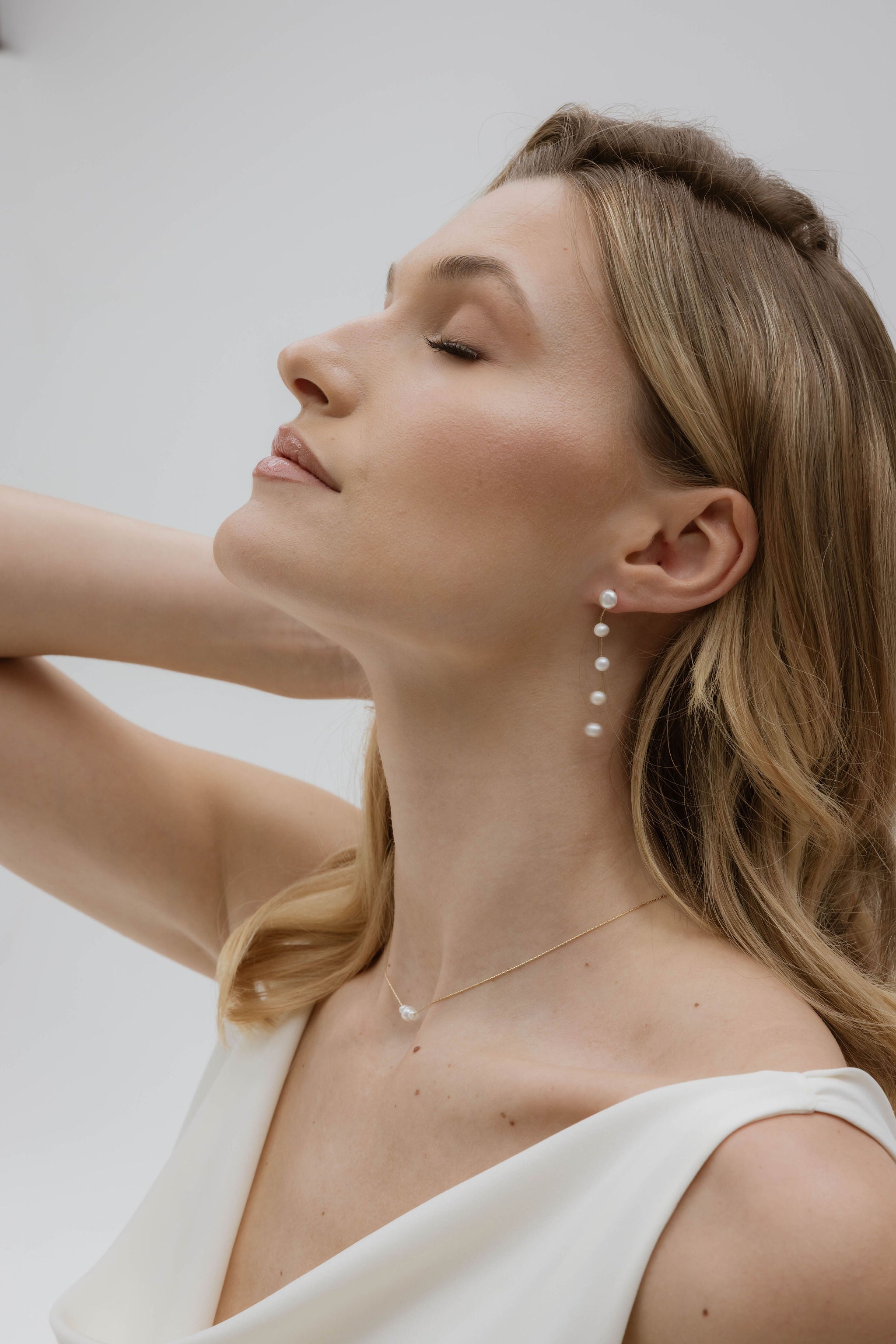 Mariée avec une robe blanche intemporelle, cheveux lâchés, parée de boucles d’oreilles et d’un collier en perles naturelles, un look simple et raffiné pour un moment inoubliable.