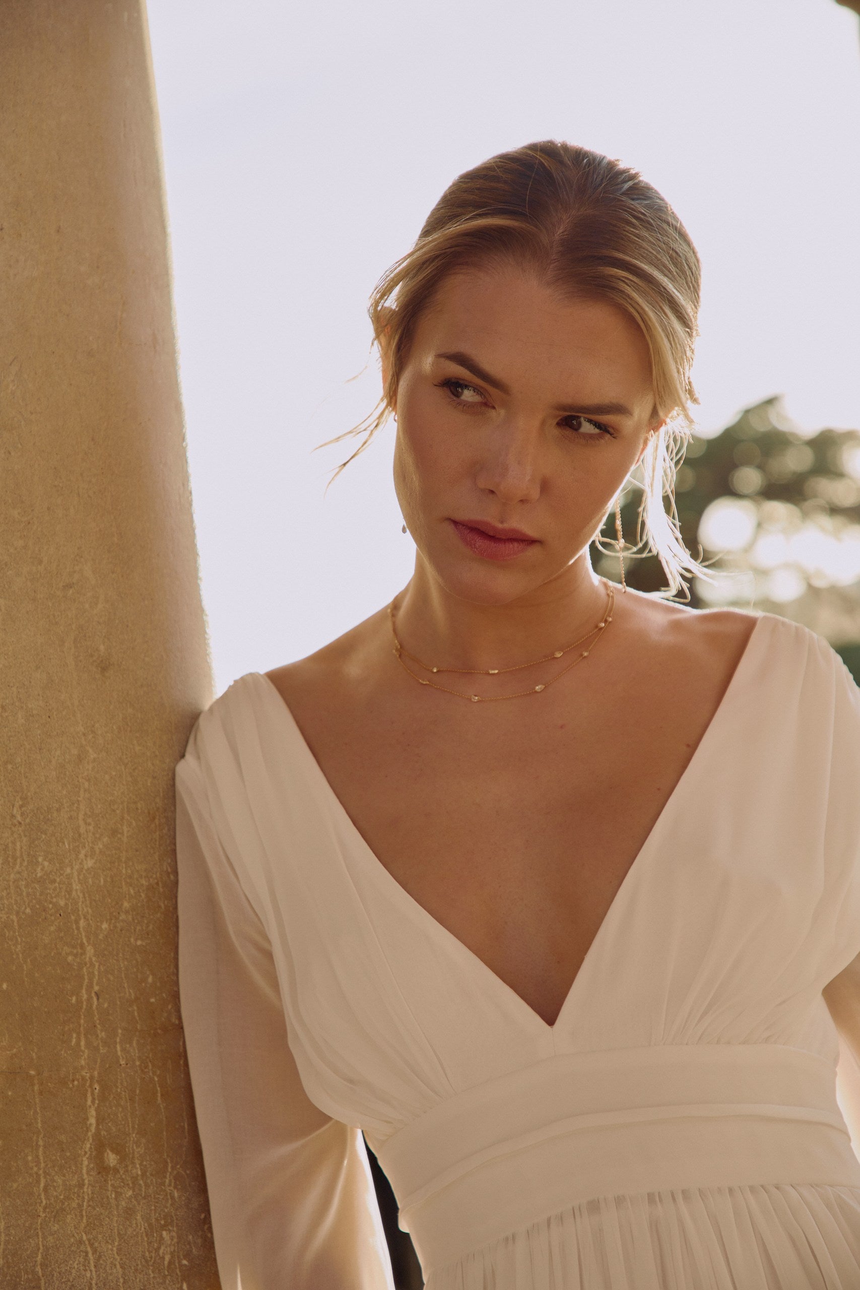 Jeune femme regardant sur le coté en portant une robe de mariée et un collier à double rang raffiné