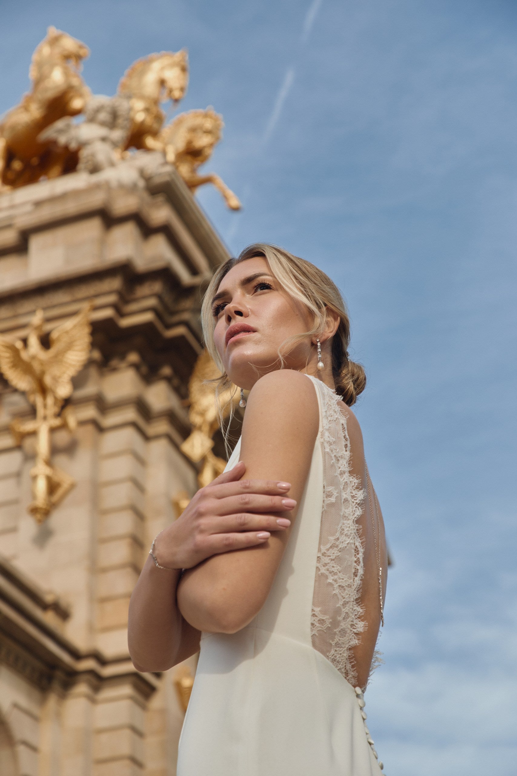 Jeune femme vu d'en bas se tenant les bras dans sa robe de mariée et ses bijoux tendance