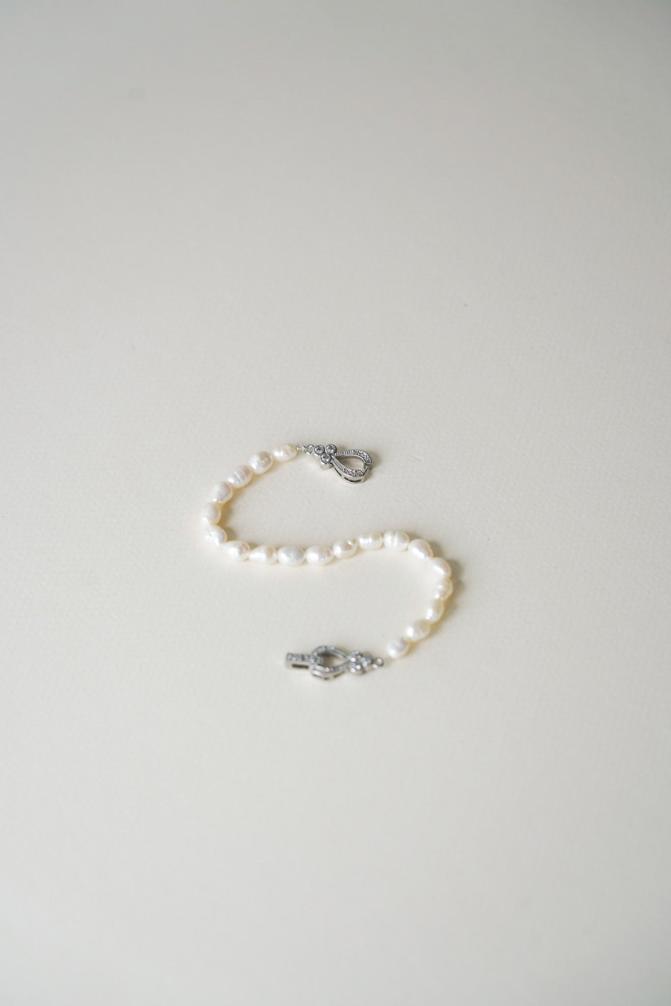 Bracelet délicat composé de perles de culture, soigneusement alignées, avec une attache dorée élégante, posé à plat sur une surface douce et lumineuse.