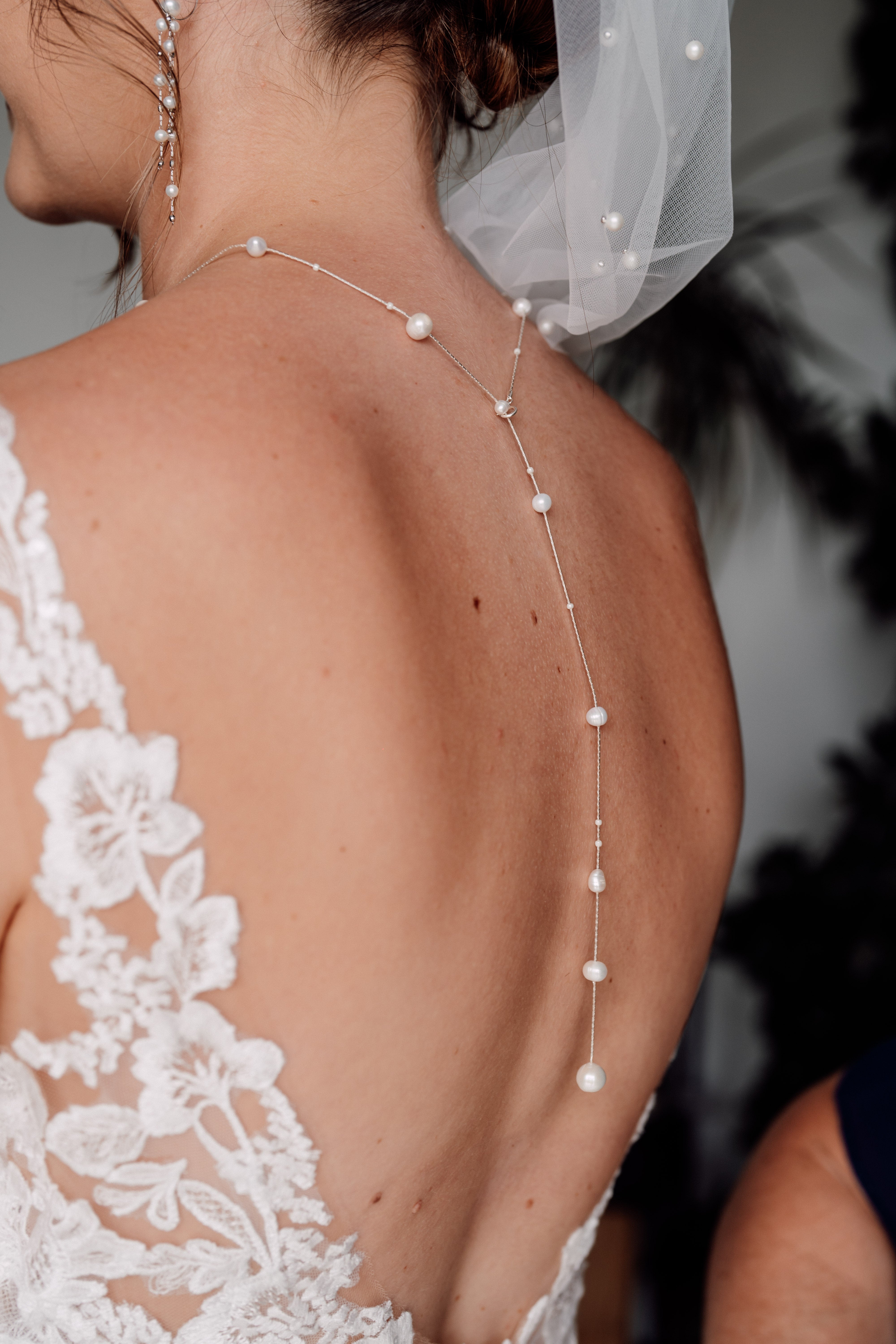 Mariée de dos avec une robe décolleté en dentelle qui porte un collier de dos avec perles Atelier Lilac