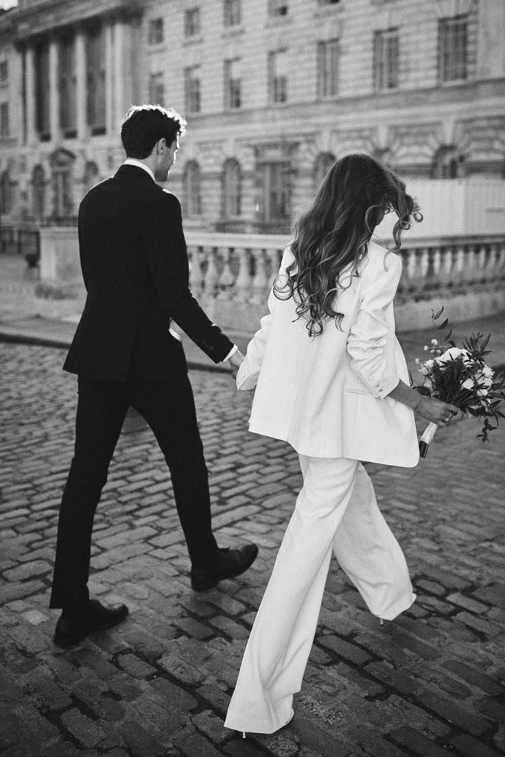 Mariées de dos qui marchent, la mariée porte un tailleur, des talons et un bouquet de mariage