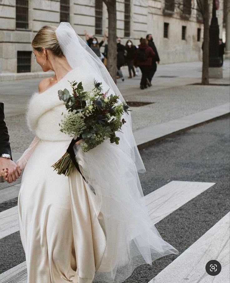 Mariee qui marche dans la rue avec une robe d'hiver, un voile long, un châle en fourrure et un bouquet hivernal
