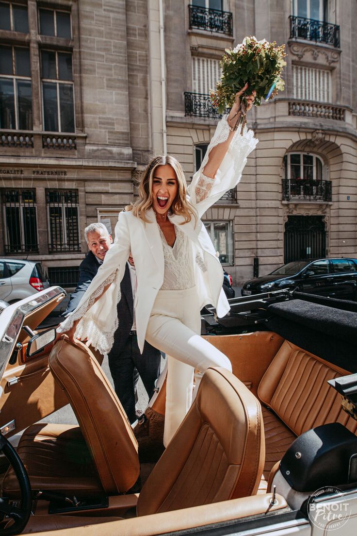 Mariée qui crie de joie après son mariage, elle monte sur la voiture et est habillée d'un tailleur de mariée et porte un bouquet