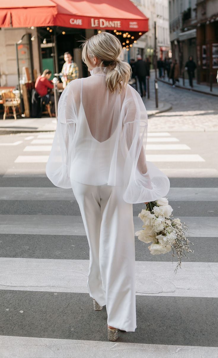 Mariée de dos qui marche avec son bouquet de mariage, elle porte un pantalon et un haut aux manches bouffantes