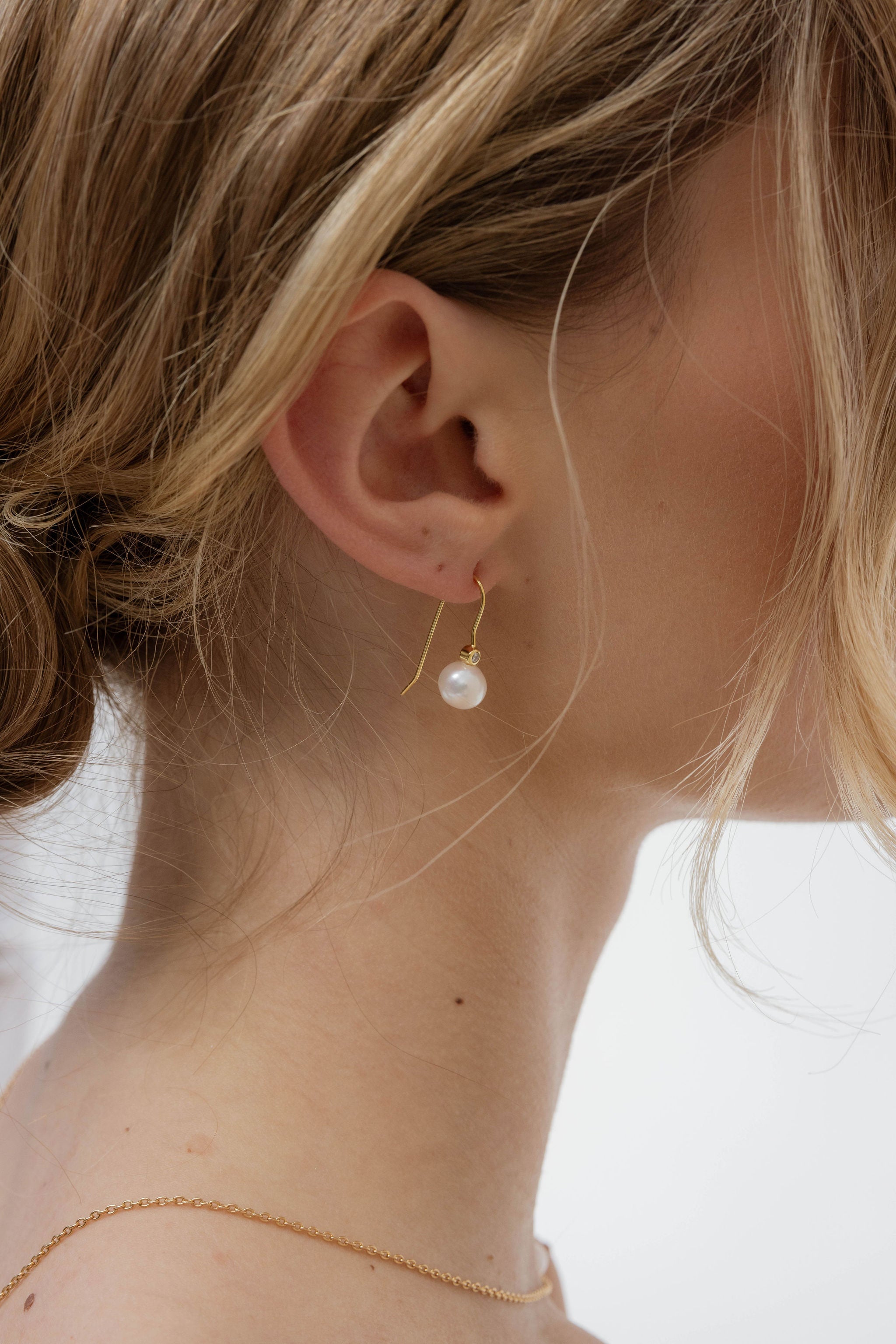 Boucles d’oreilles courtes et minimalistes, composées d’une perle et d’un petit diamant, au design doux et raffiné, idéales à porter avec un chignon ou les cheveux lâchés