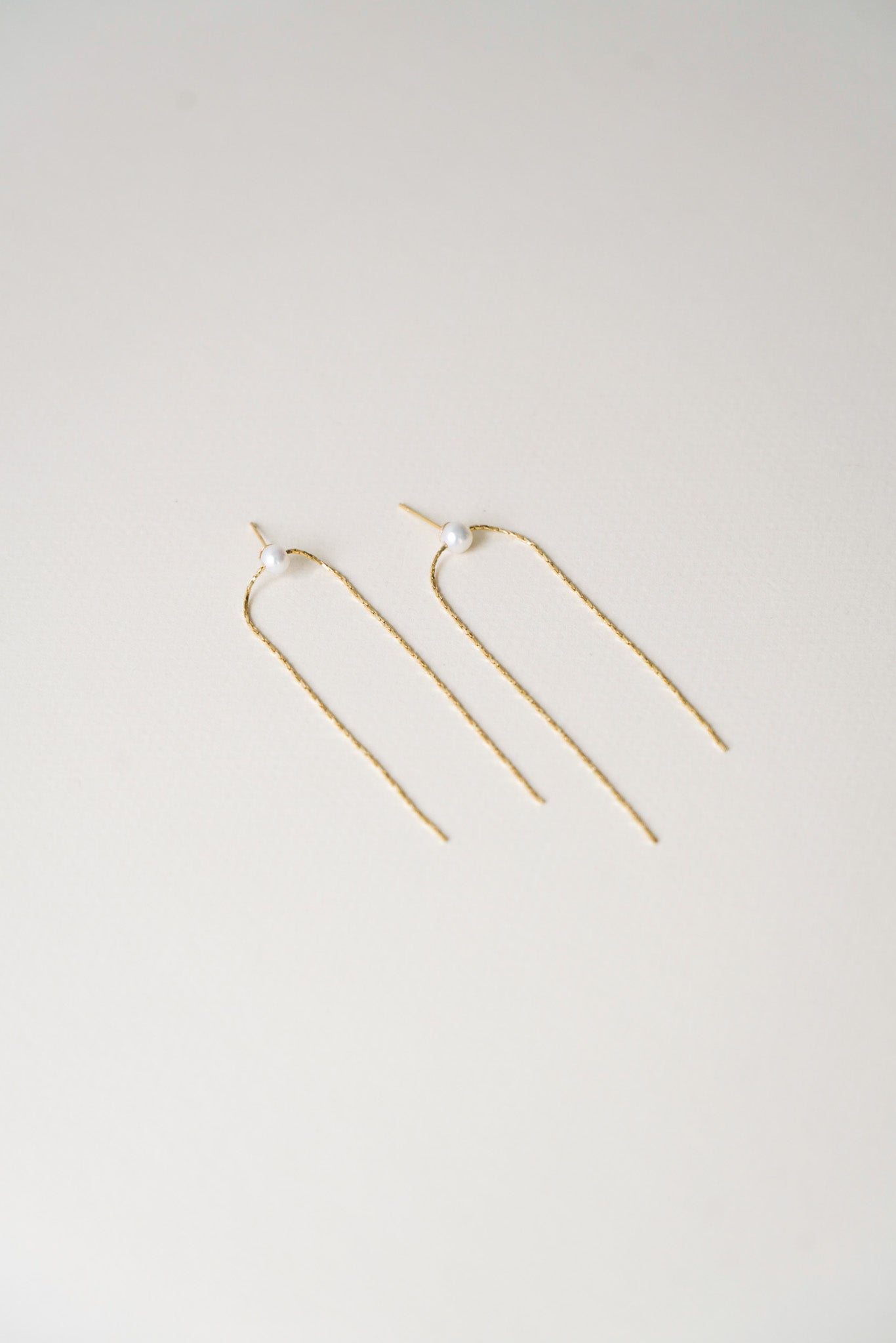 Boucles d’oreilles délicates composées d’une fine chaîne en or, très légère et élégante, avec une perle de culture blanche placée au niveau du lobe de l’oreille. La chaîne fine descend des deux côtés, apportant un équilibre subtil et un style raffiné, parfait pour un look minimaliste et chic.